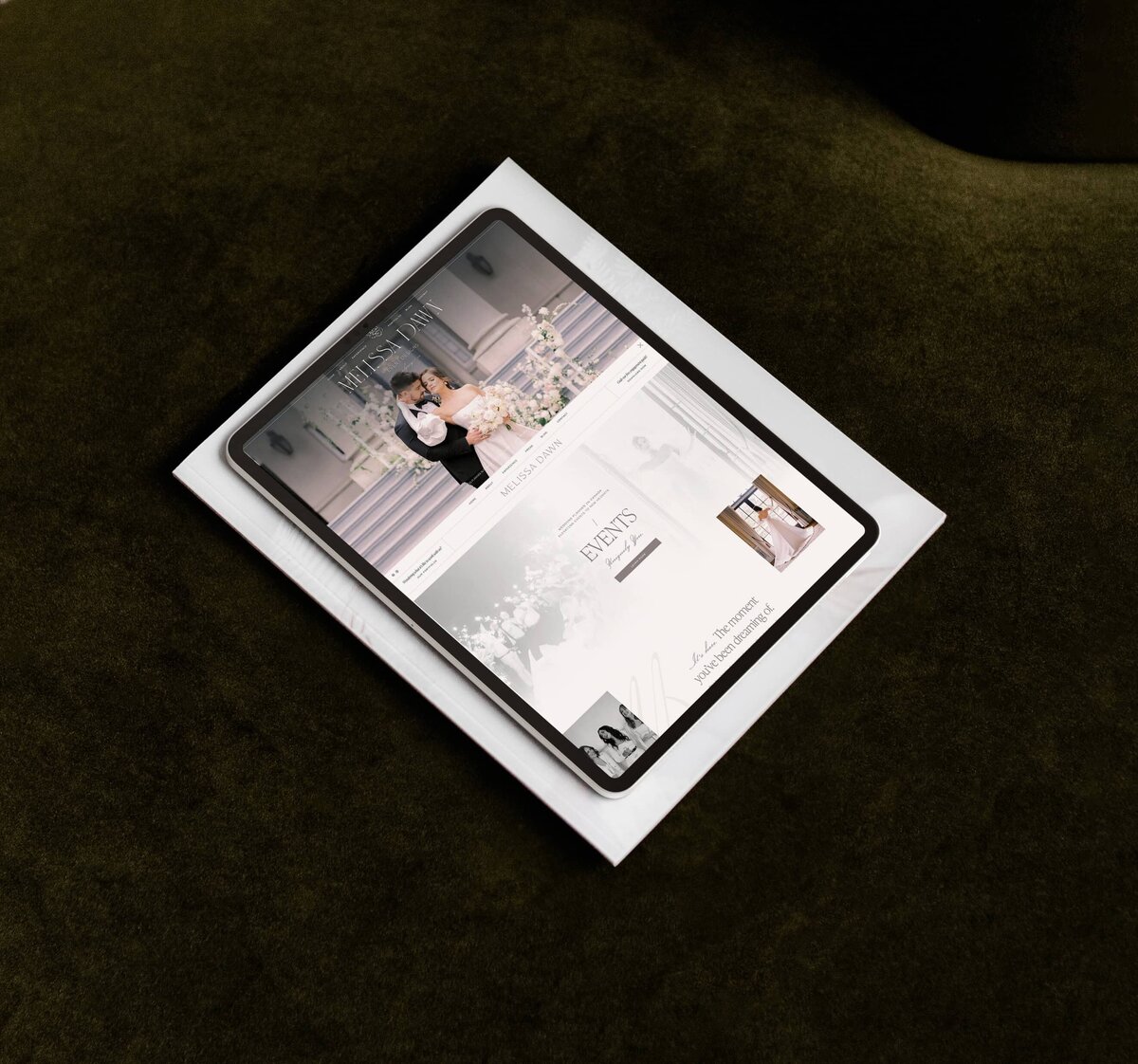 A tablet displaying a wedding planner branding and website with images of a couple, event details, and decor, placed on top of a white magazine on a dark green surface. The elegant showit web design for luxury wedding planners enhances the browsing experience.