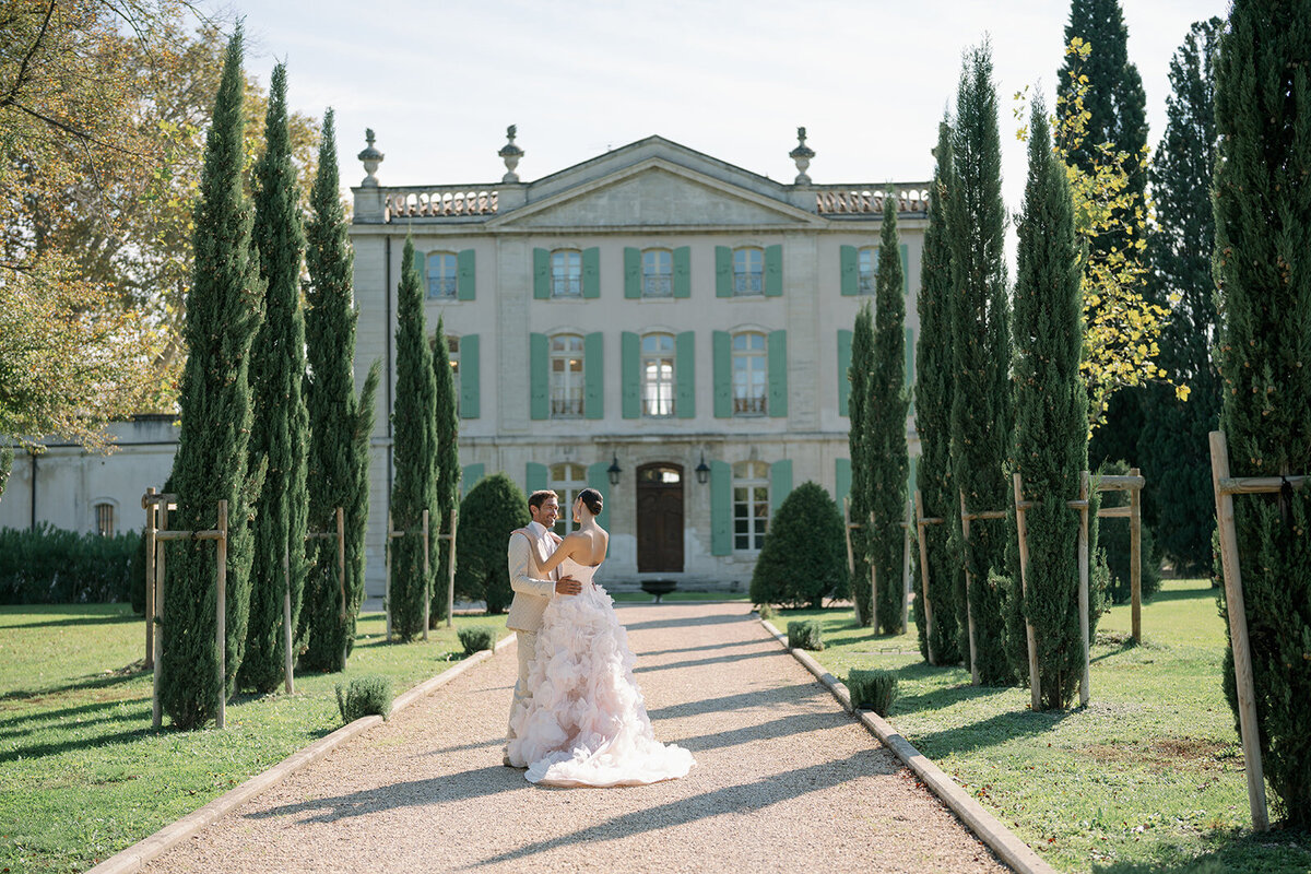 Bride and groom walking down tall cypress-lined pathway leading to Château de Tourreau in Provence France.