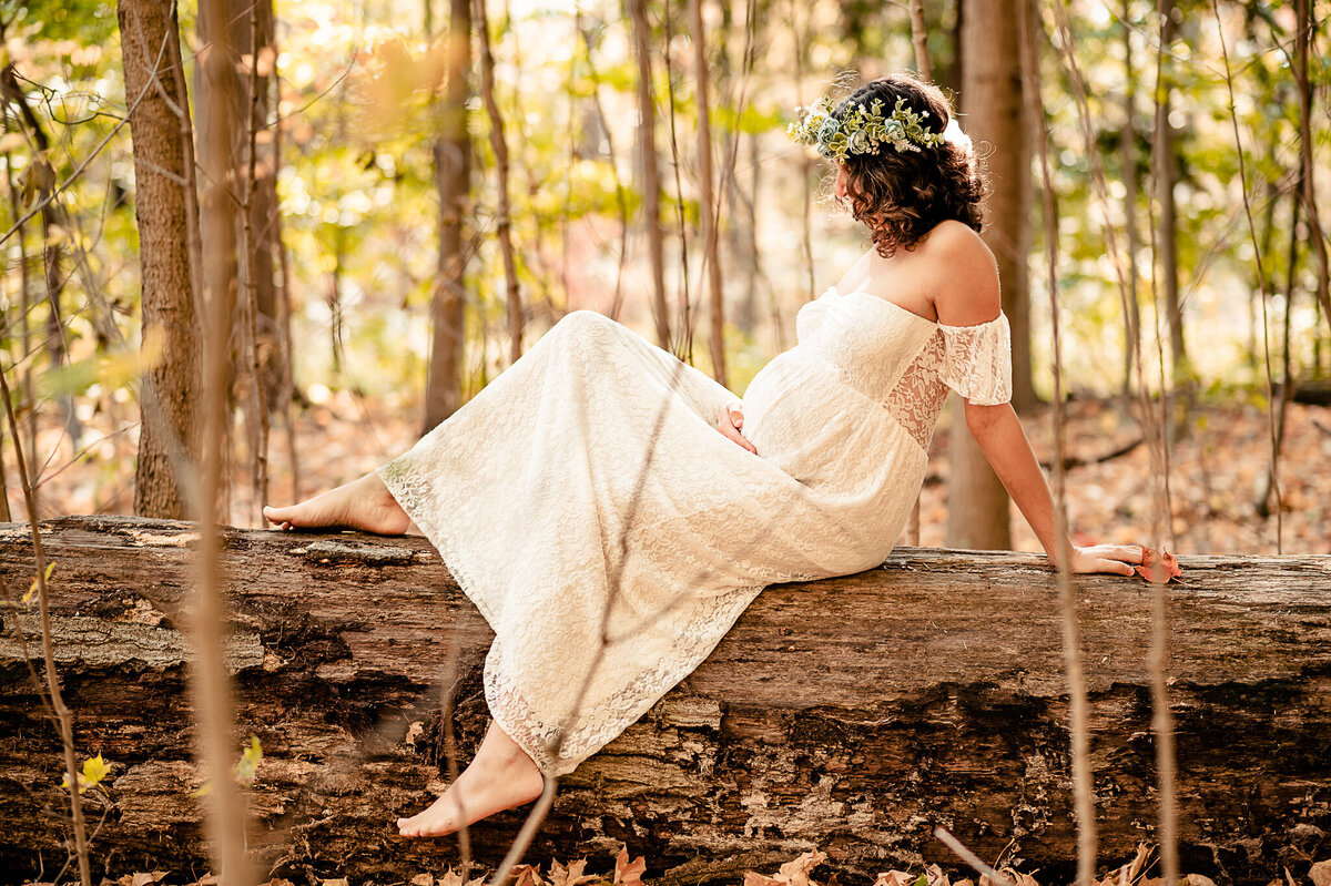 Glamorous mom to be in a forest wearing a lace dress sitting on a log at Beamer Memorial Conservation.