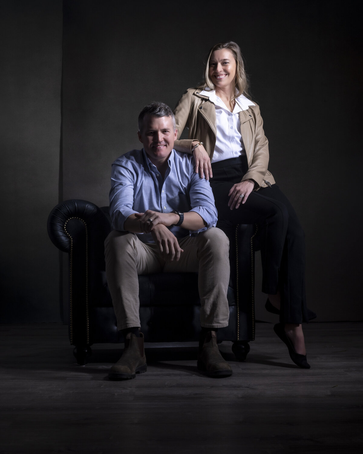 Professional duo portrait in CT of a man and woman seated together in a dark studio setting, ideal for branding and business headshots in CT and MA, by Rob Faber Photography.