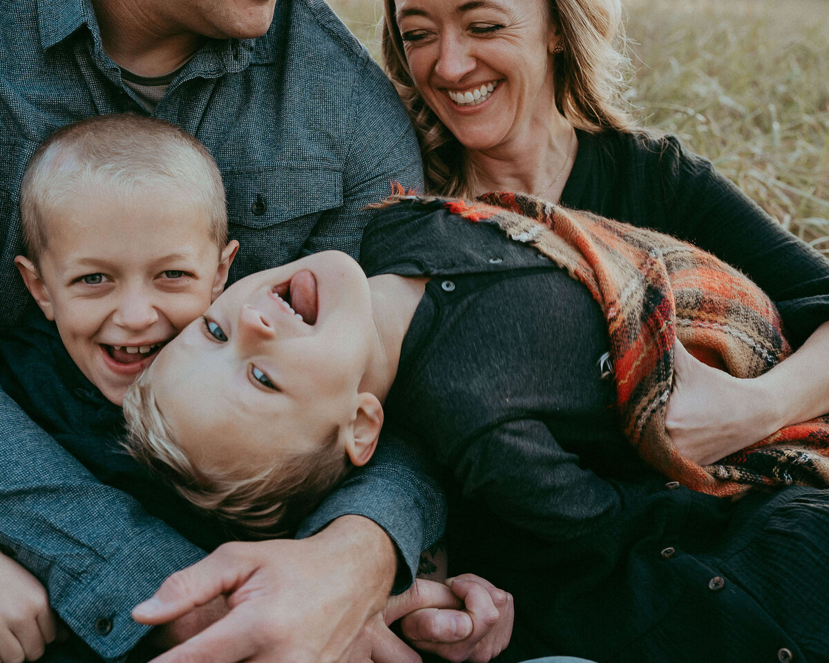 The youngest of three boys goofily flings himself across his families lap during a fall golden hour session in Denver.