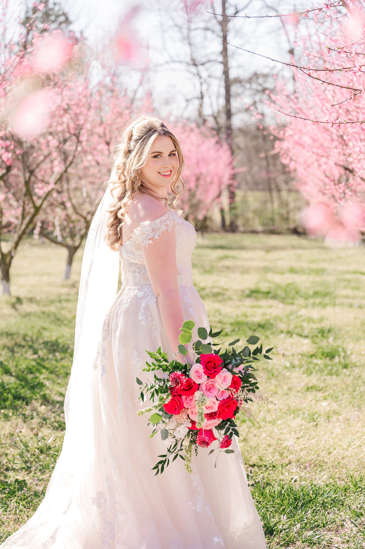 A stunning blonde bride walking in pink and red cherry blossoms at sunset enjoying her destination wedding photography session