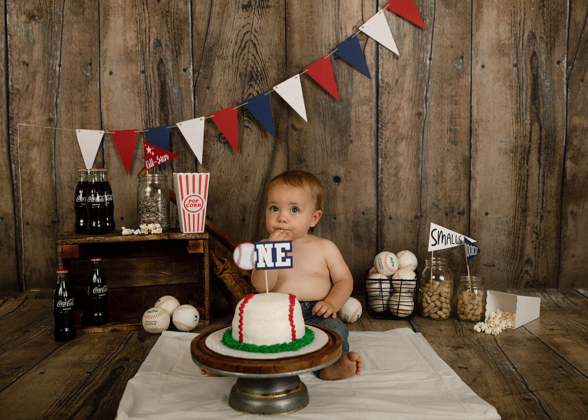 1 year old boy eating a baseball cake. Baseball decorations surround him.