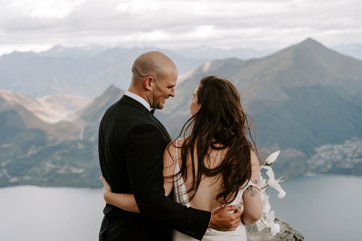 The Lovers Elopement Co - bride and groom look out over mountain top wedding venue in Queenstown, New Zealand