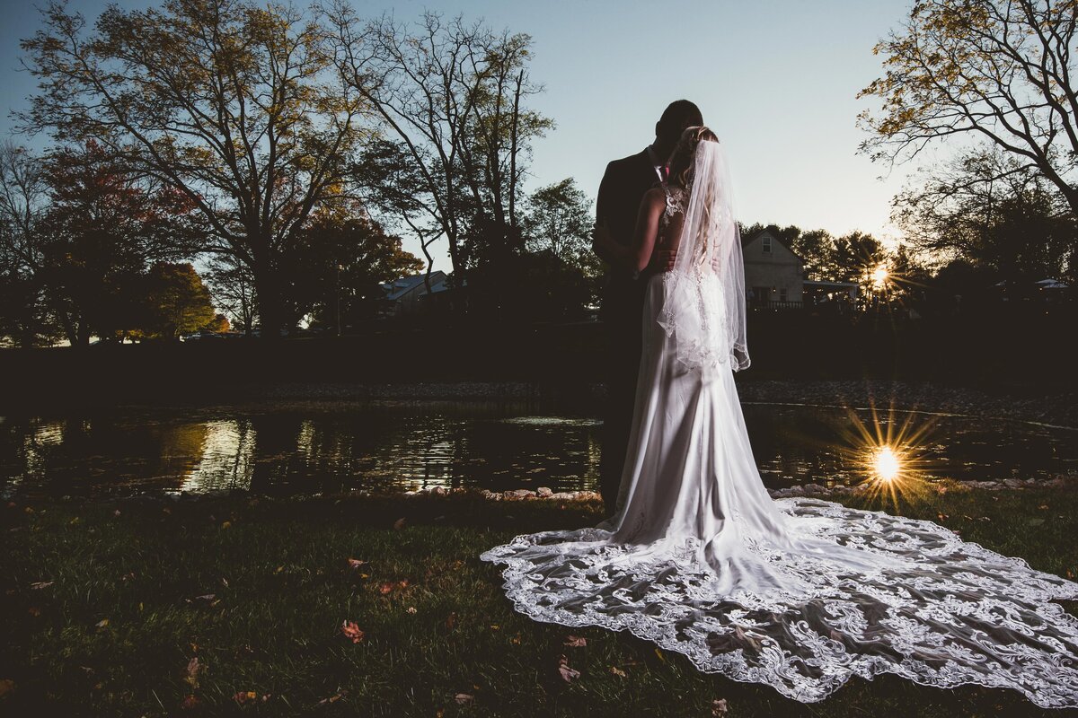 a bride and groom hold one another in an image shot in front of a fading sunset