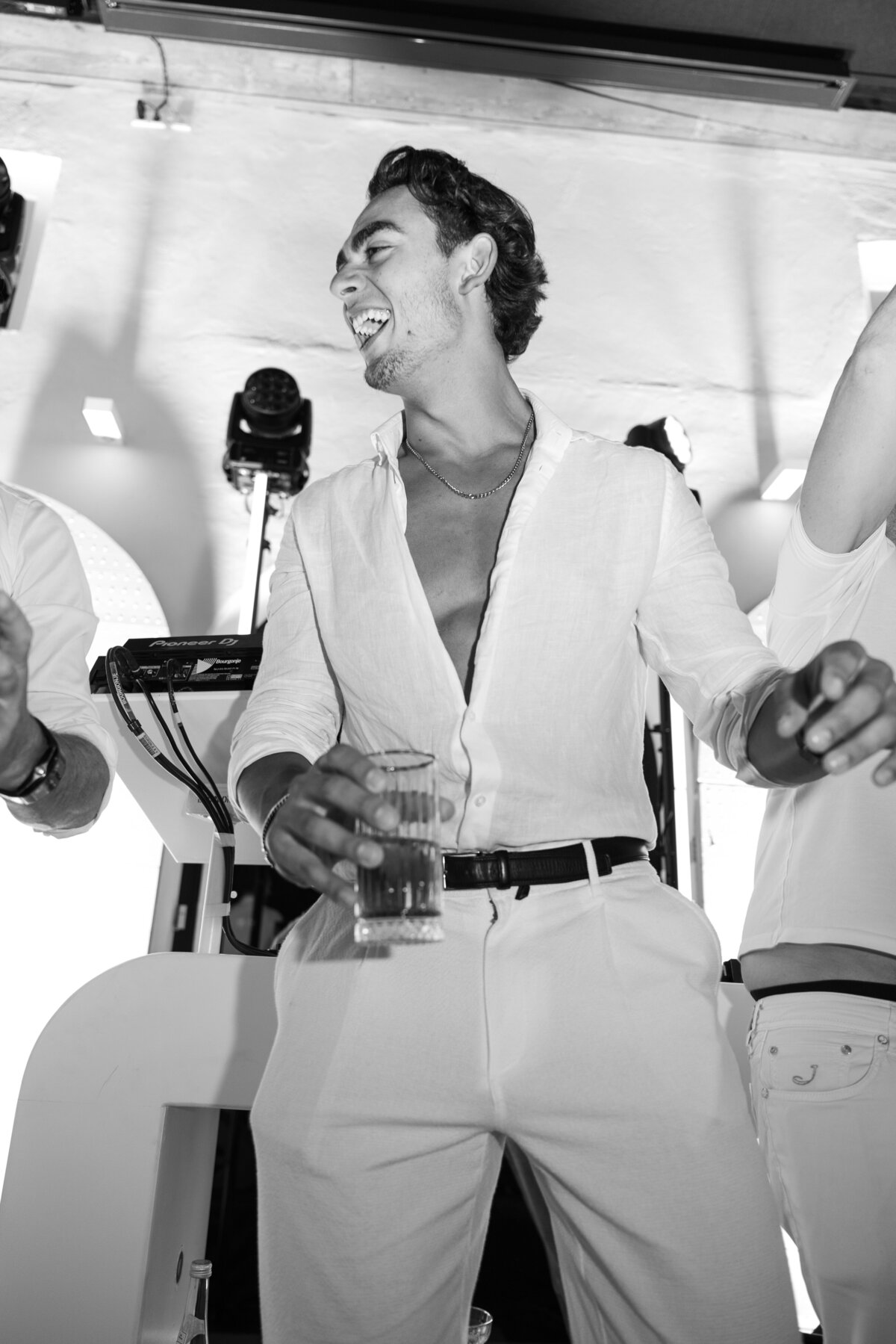 A young man laughing exuberantly during a party on a luxury yacht, dressed in a casual white outfit. This black-and-white image captures the joy and energy of the event.