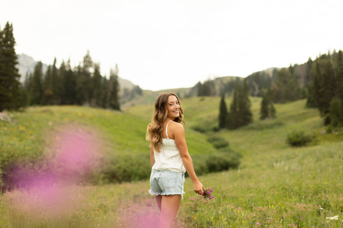 Young woman sits on rocks in a field with large trees as she rests her elbow on her knee.