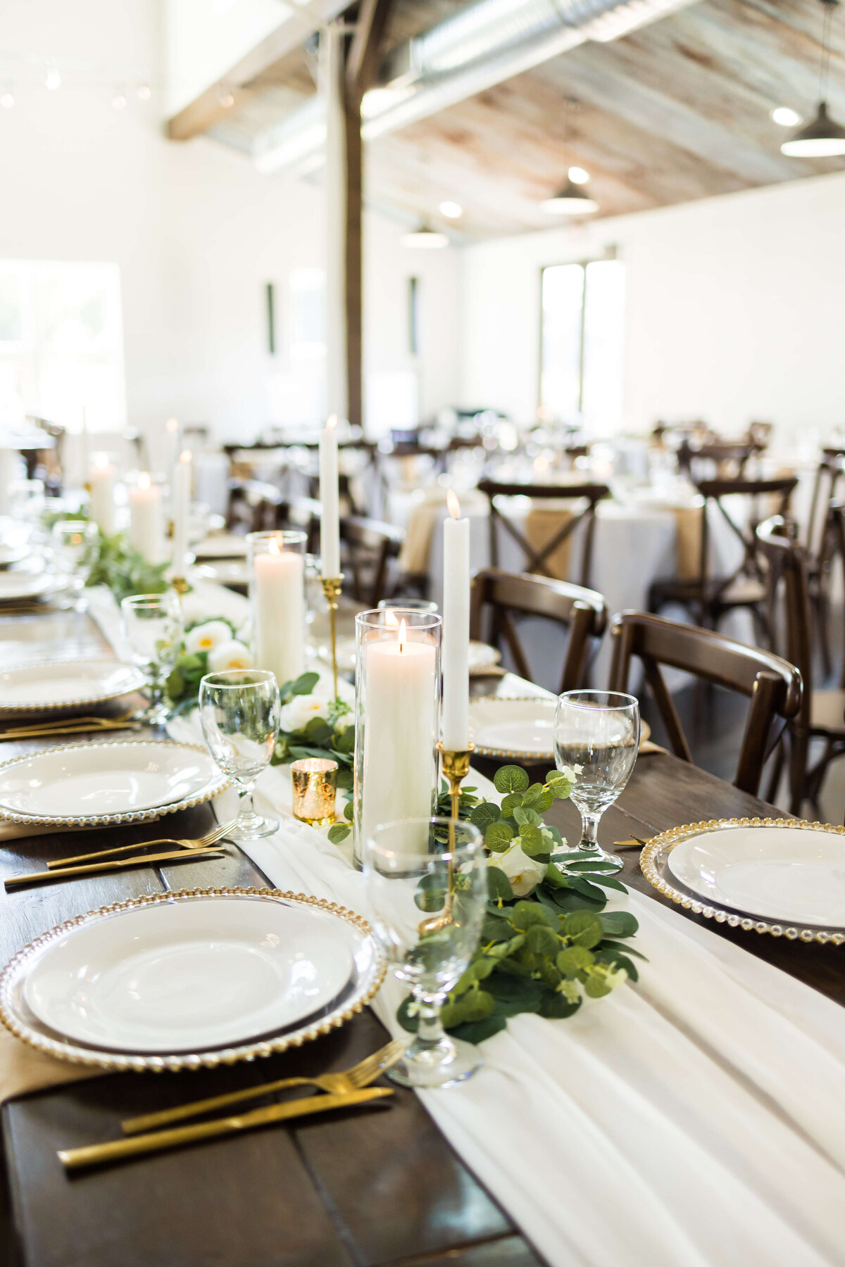 Wedding reception table set up with candles and greenery and gold flatware