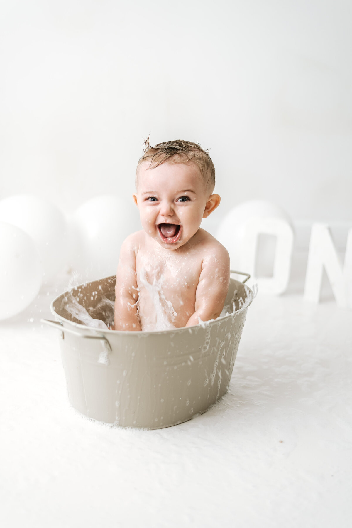 Baby boy in the bath splashing bubbles at cake smash photoshoot in Billingshurst