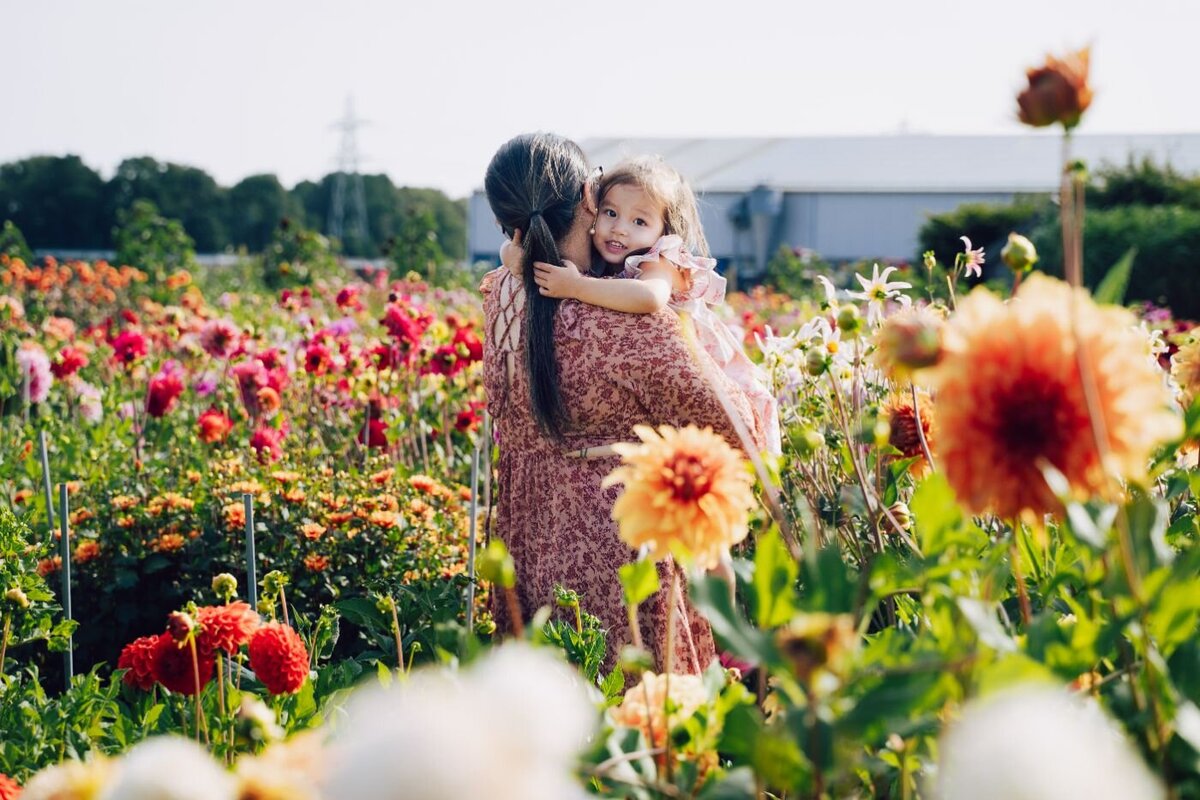Little girl hugging her mother among colorful blooming flowers in a sunny Rotterdam flower field.
