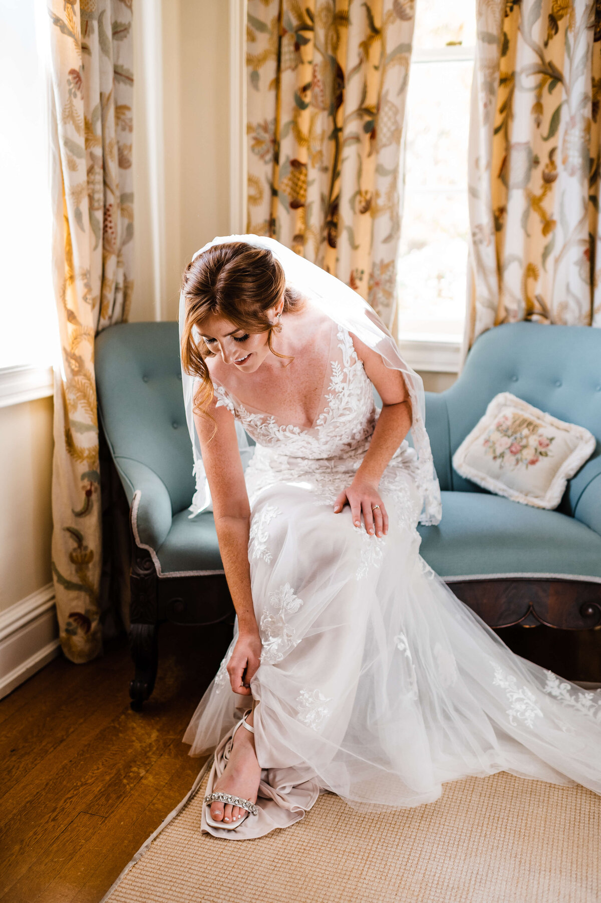 wedding photos with bride putting on her heels while sitting on a blue couch in a bridals suite at Charlotesville wedding venues Murray Hill