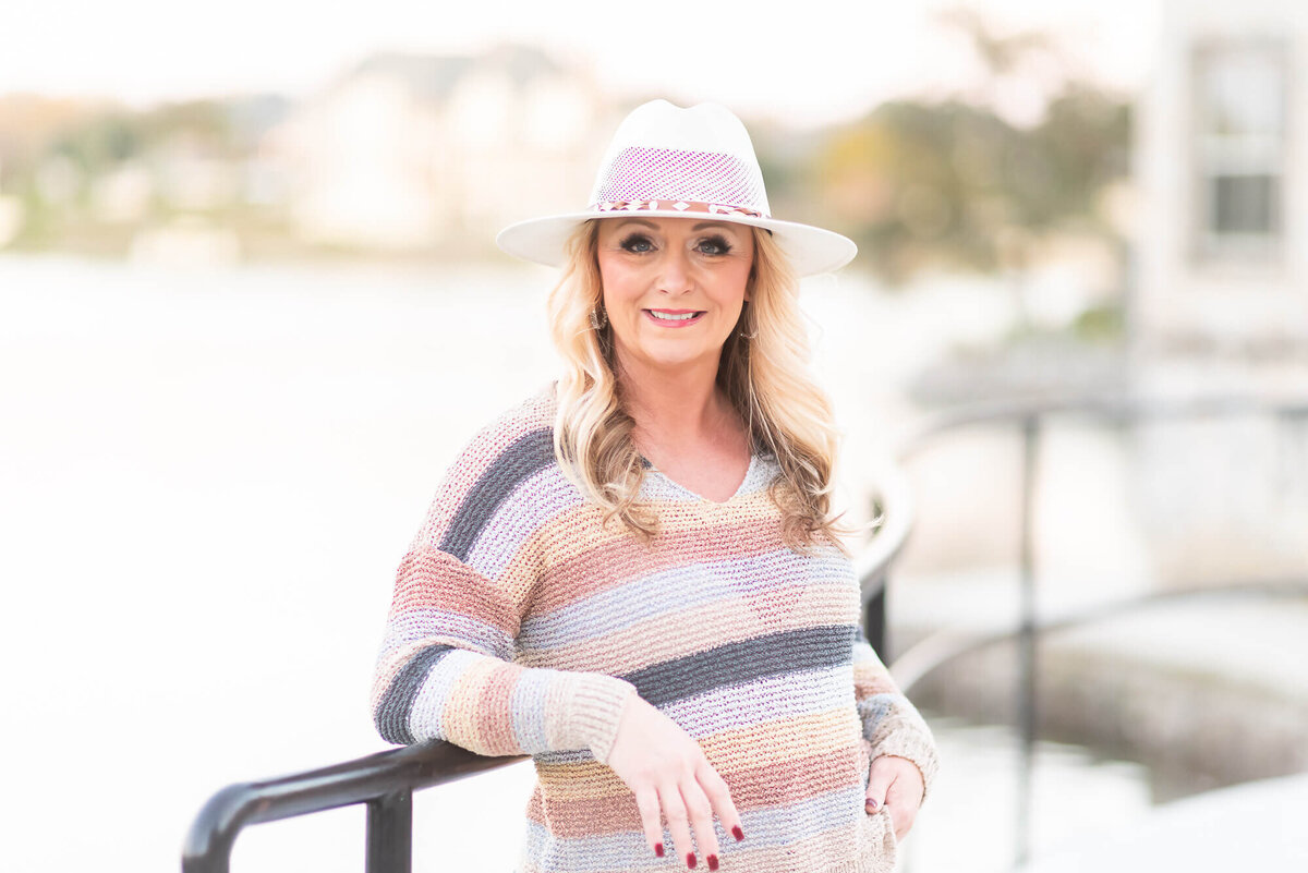 woman in striped sweater and white hat leaning against a rail by the water