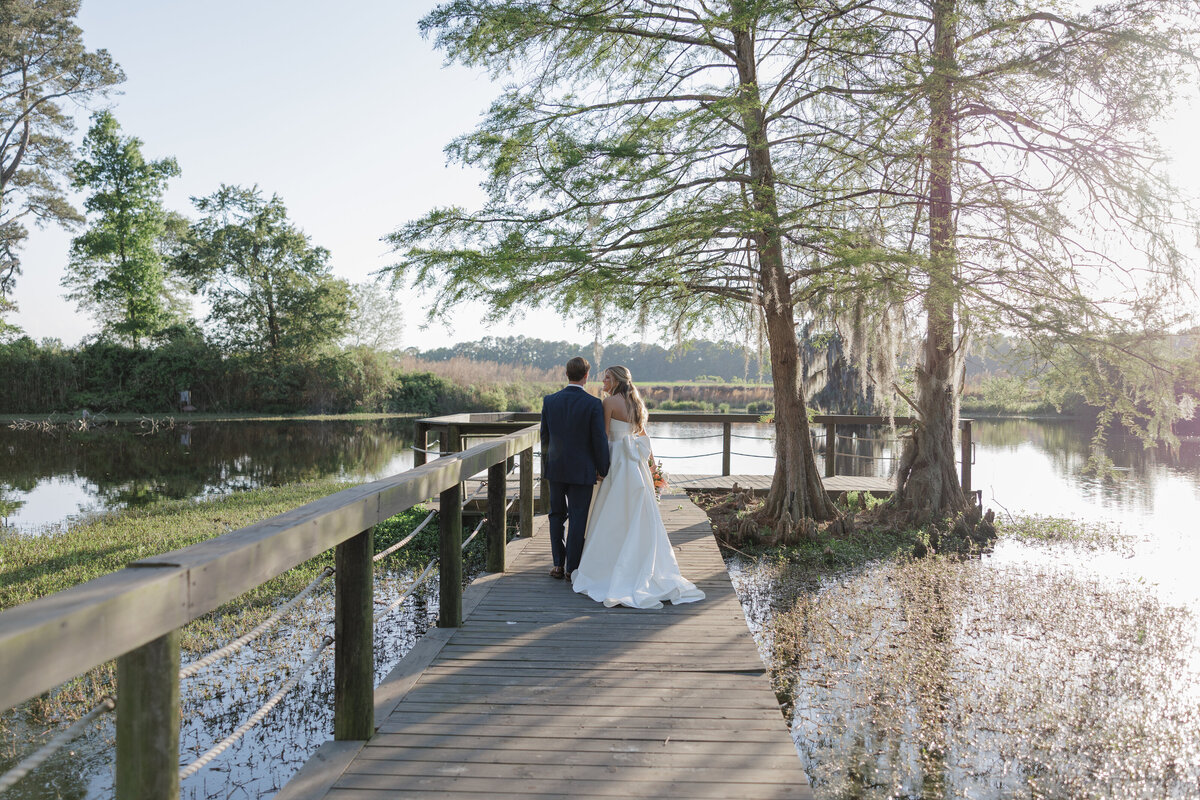 Bride and Groom walk through a field at sunset while groom holds the bride's dress at Thornblade Country Club in Greenville,SC