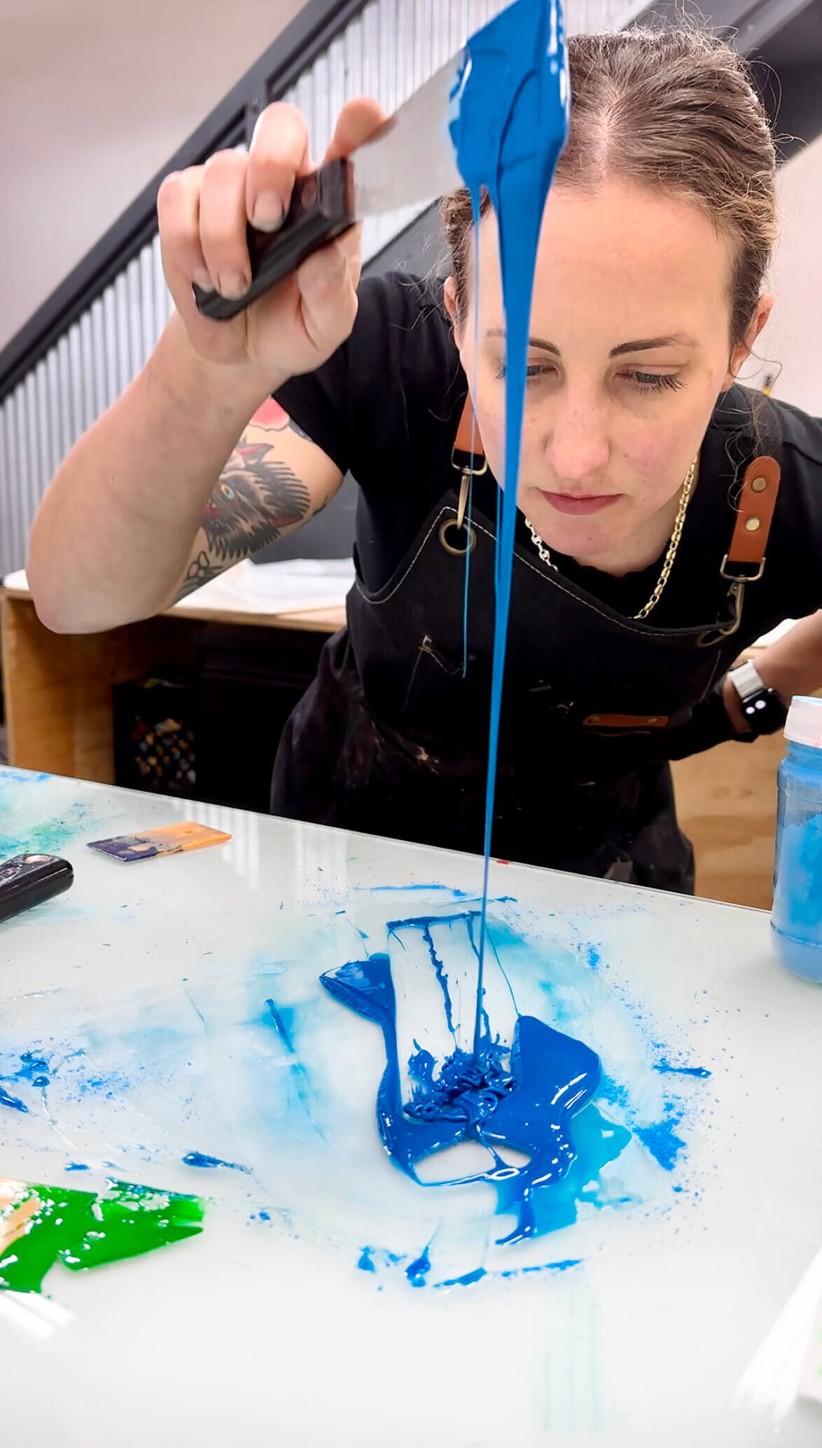 Printmaker Courtney Sennish—mid-process and full of focus—pours freshly mixed blue ink from a palette knife while inspecting its consistency.