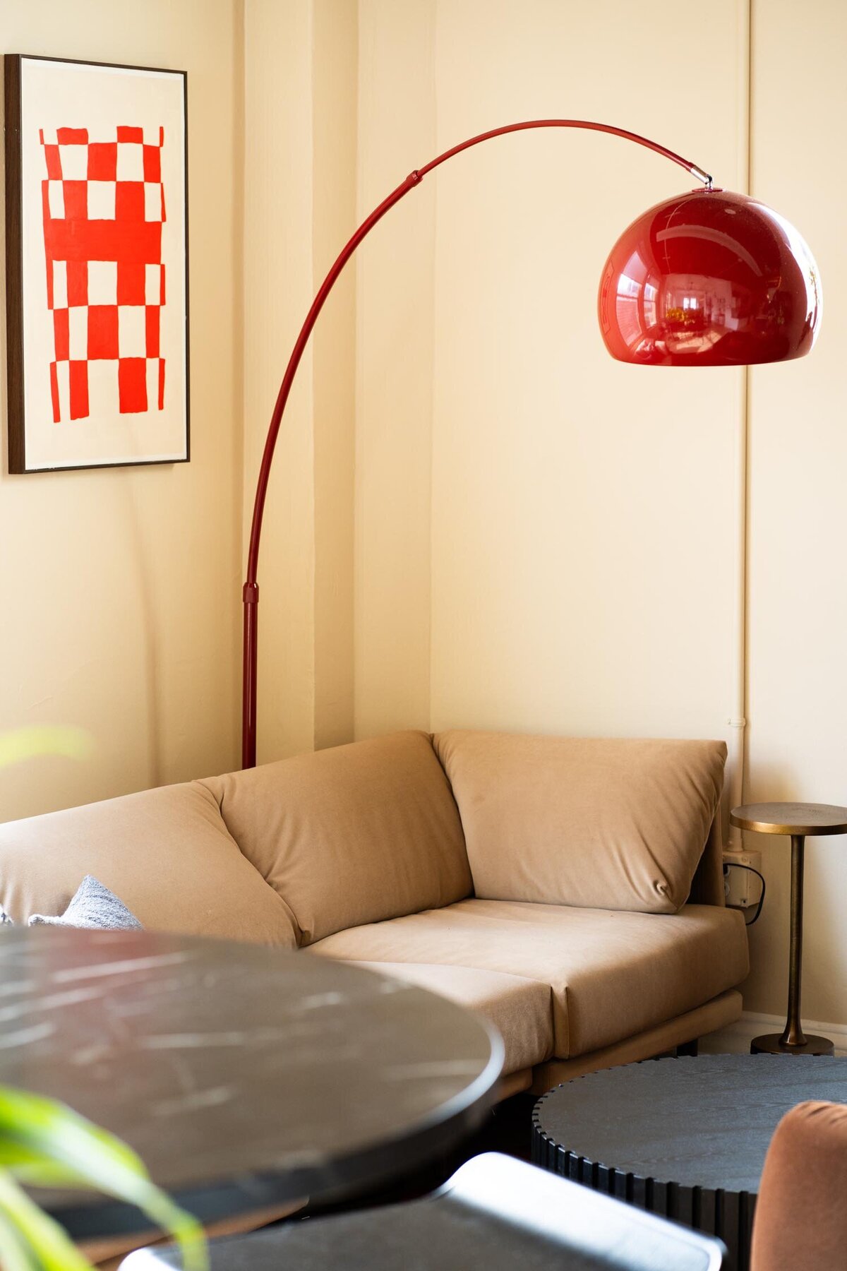 Beige corner sofa paired with a red arched floor lamp and minimalist red artwork in a softly lit lounge area.