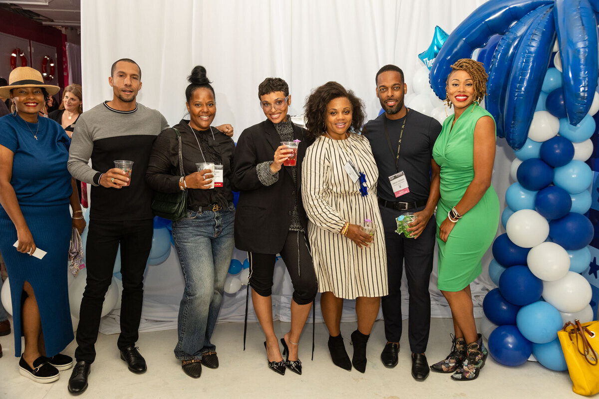 Group of six people posing with drinks in front of balloon decor