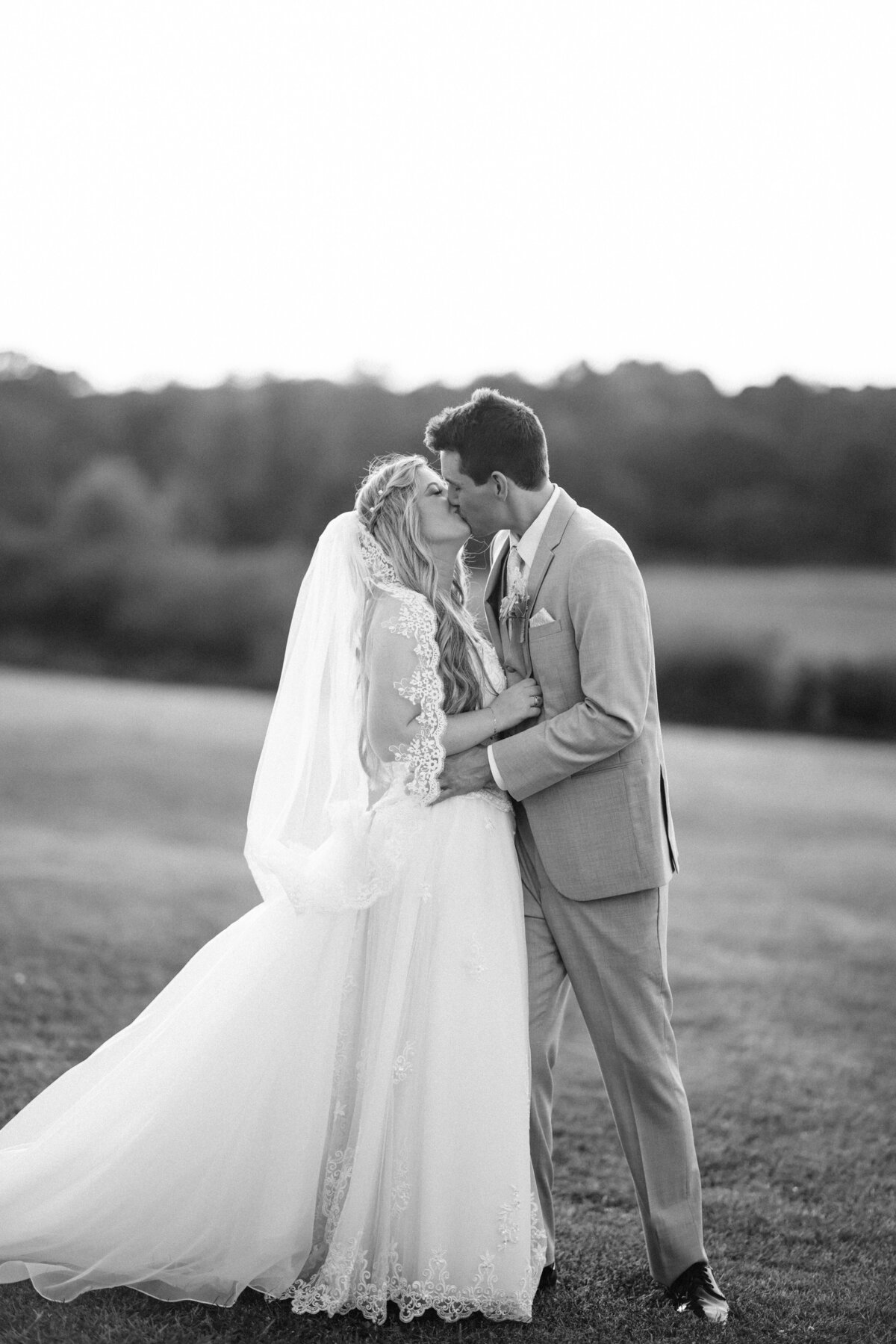 Black & White candid photo of bride & groom sharing a kiss in the fields of West Milford Farm, Cumming, GA. 