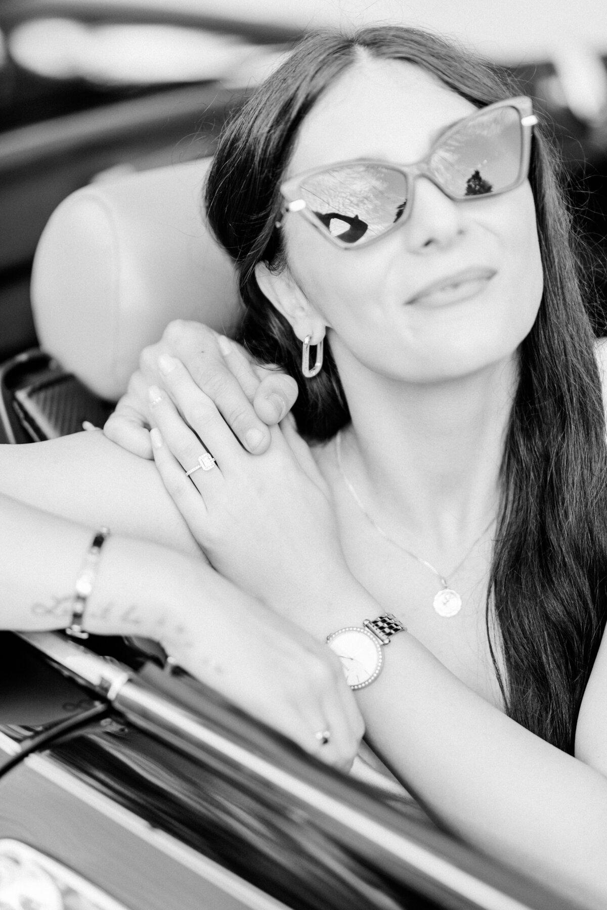 Bride-to-be in classic cat-eye sunglasses, leaning back in a vintage car, her engagement ring sparkling on her hand