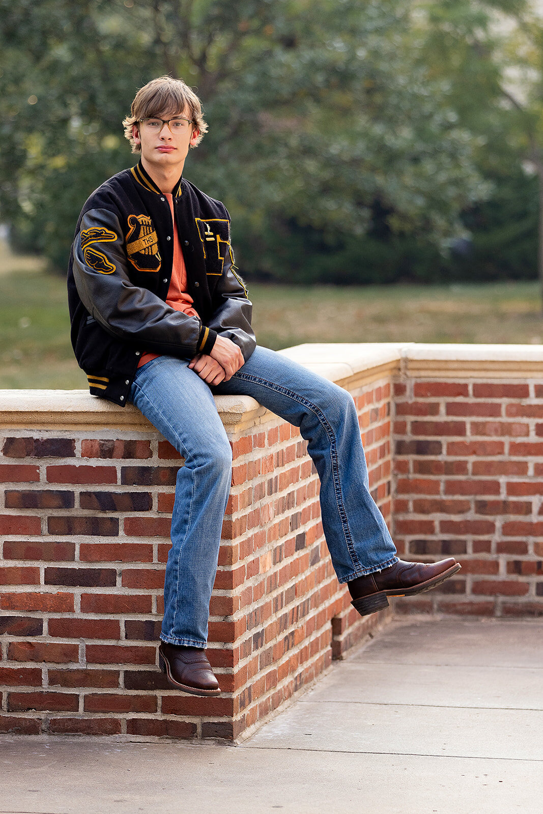 boy on brick wall at school wearing letter jacket and boots