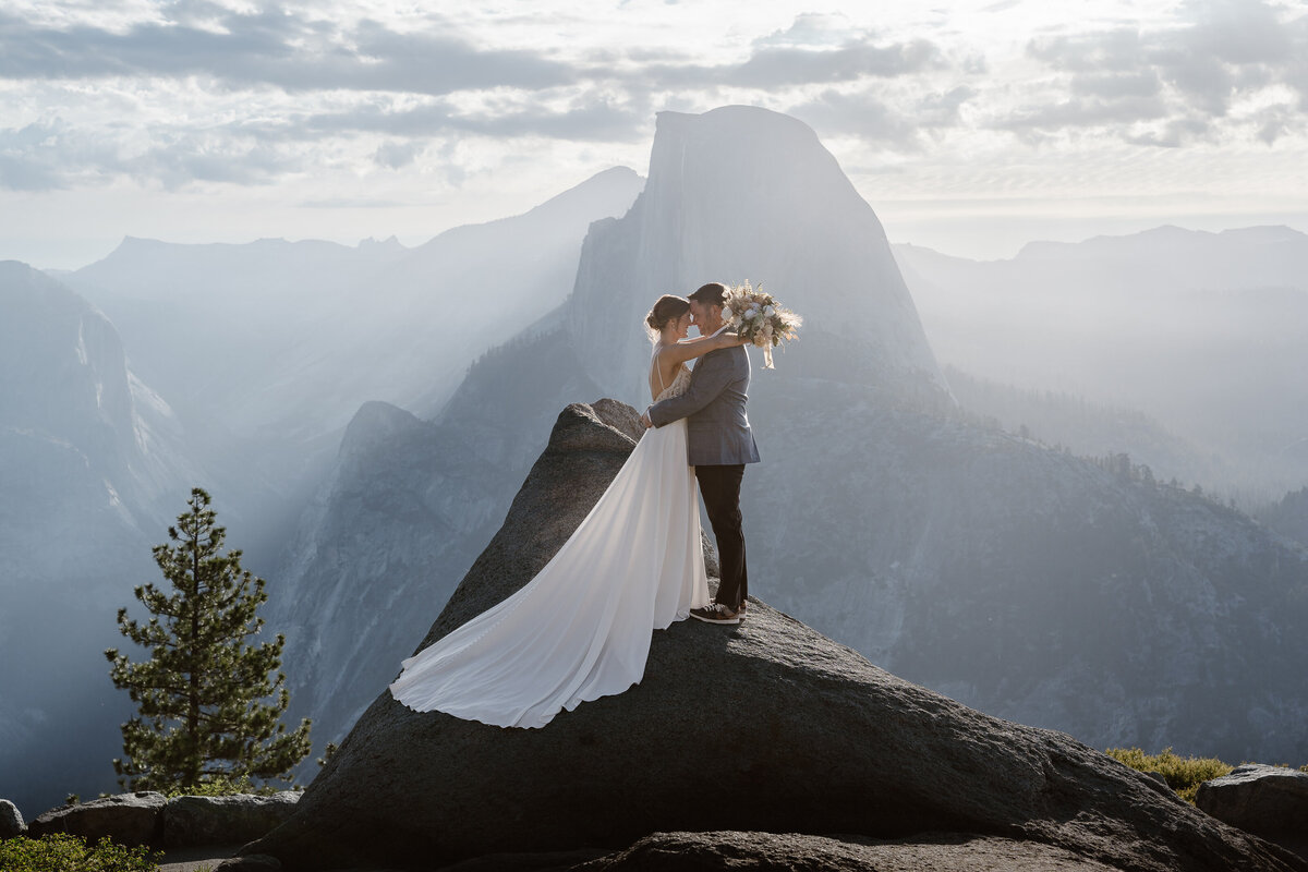 A couple standing close together on top of a rock with Half Dome in the distance
