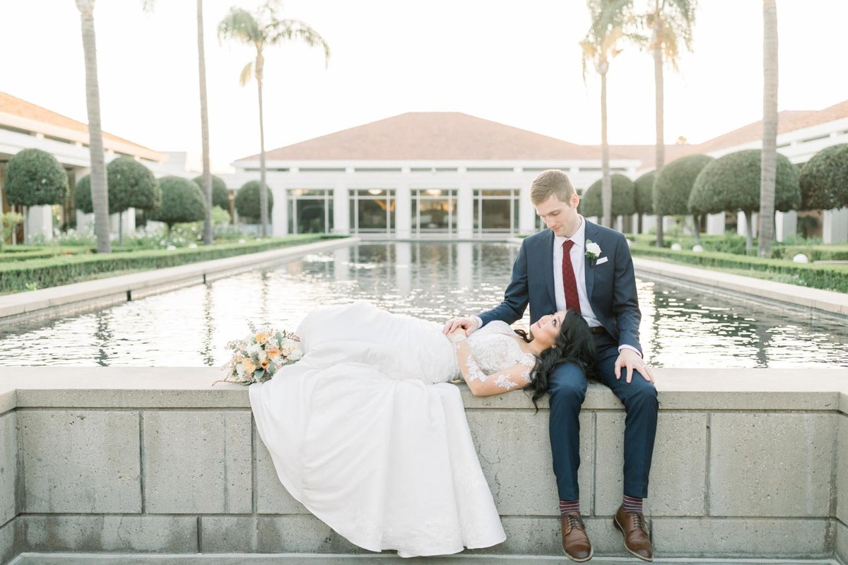 Bride lays her head on the Groom's lap while laying on the brick wall that surrounds the reflection pool at the Richard Nixon Library