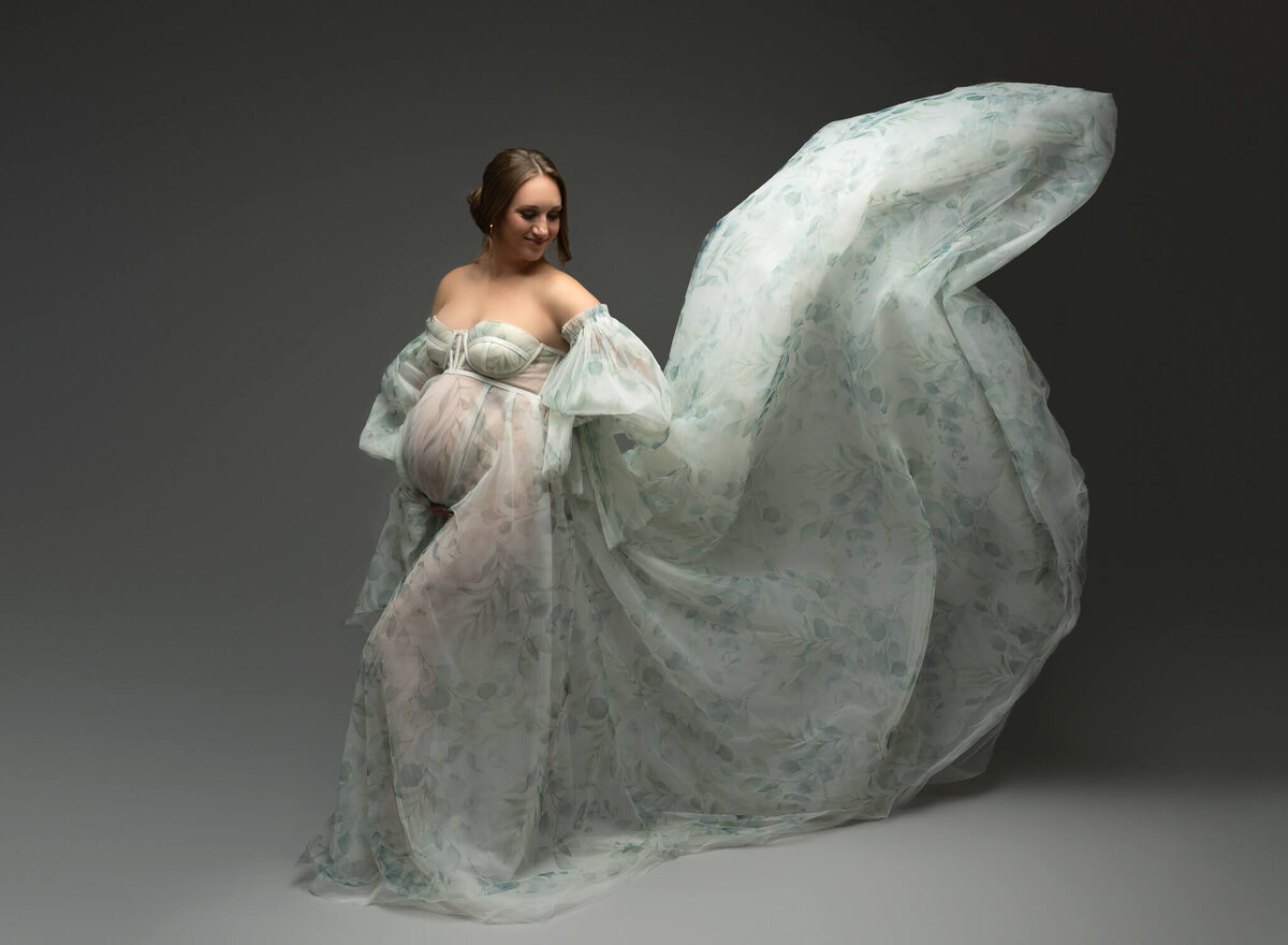 pregnant woman wearing flowing green and white floral maternity dress during photoshoot