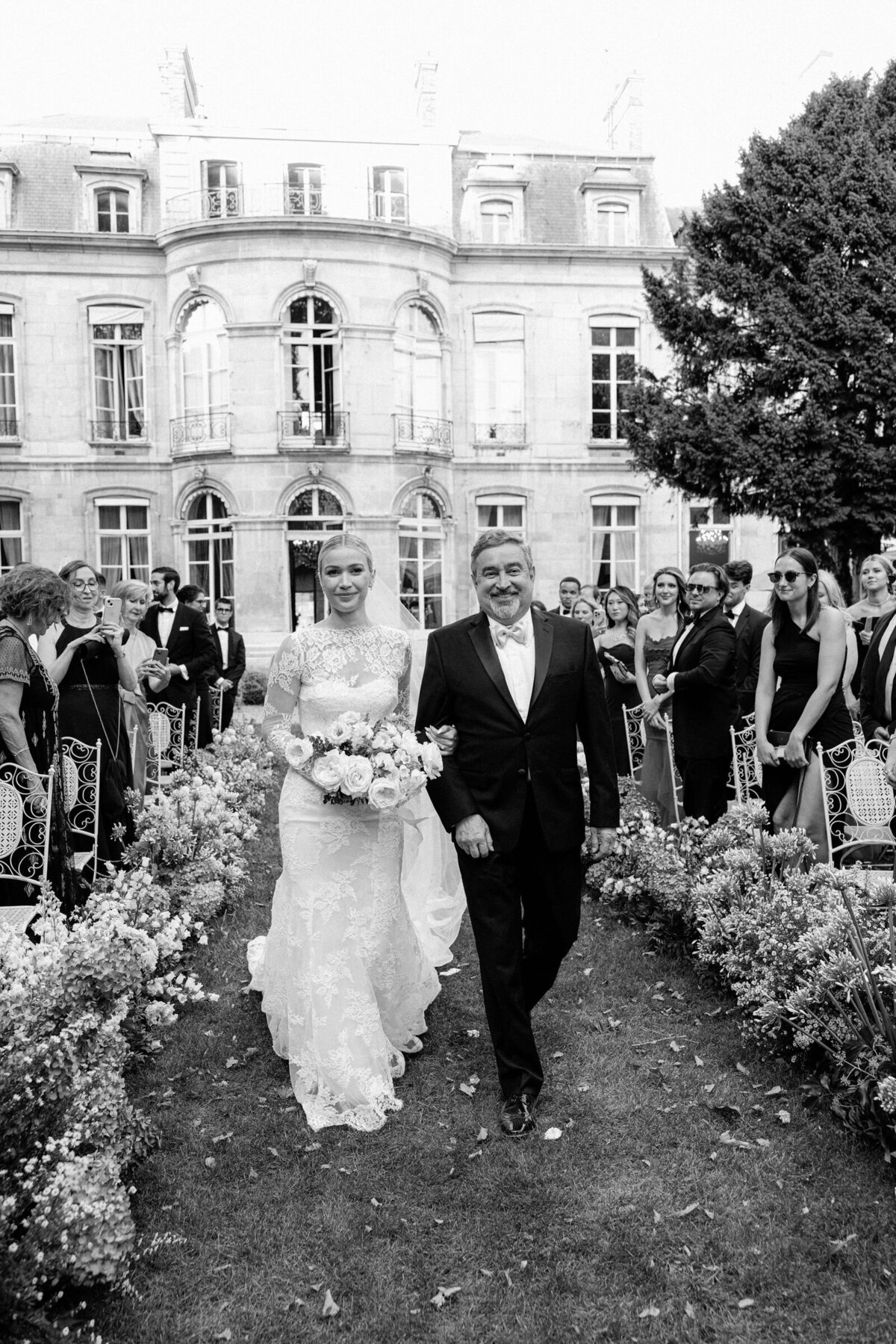 Bride walks down the aisle with her father while all guests cheer for them.
