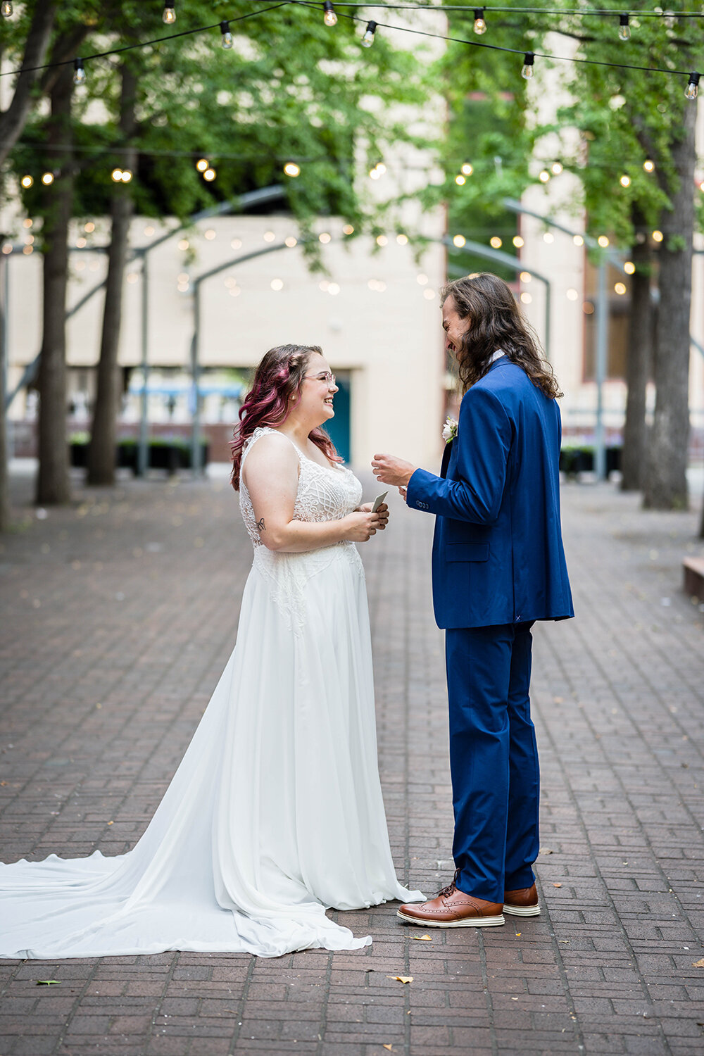 A wedding couple smiles widely at one another as they prepare to read their vows on their elopement day in a secluded, private, tea-lit alleyway in Roanoke, Virginia.