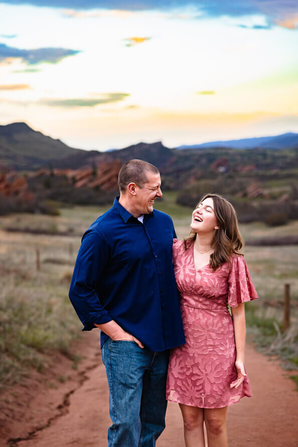 A dad laughs with his teenage daughter with Red Rocks Park in the background.