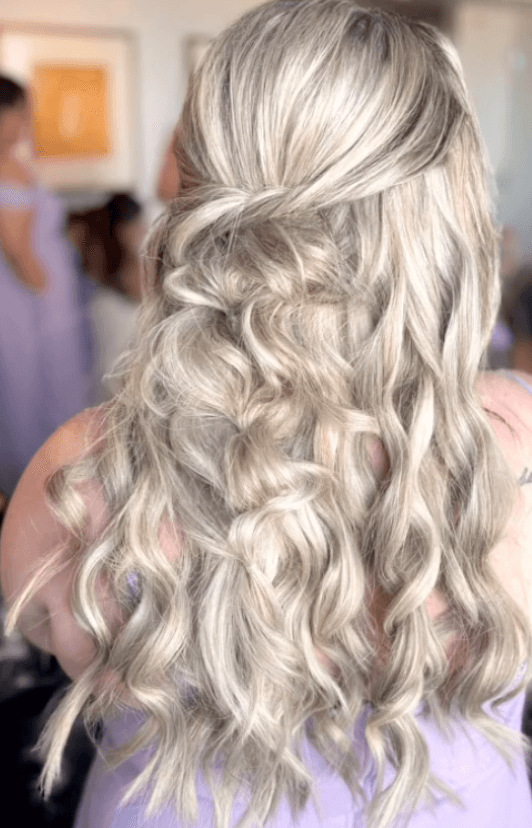Back view of long blonde hair styled in soft curls with a twisted half-up braid, created for wedding party hair in San Antonio