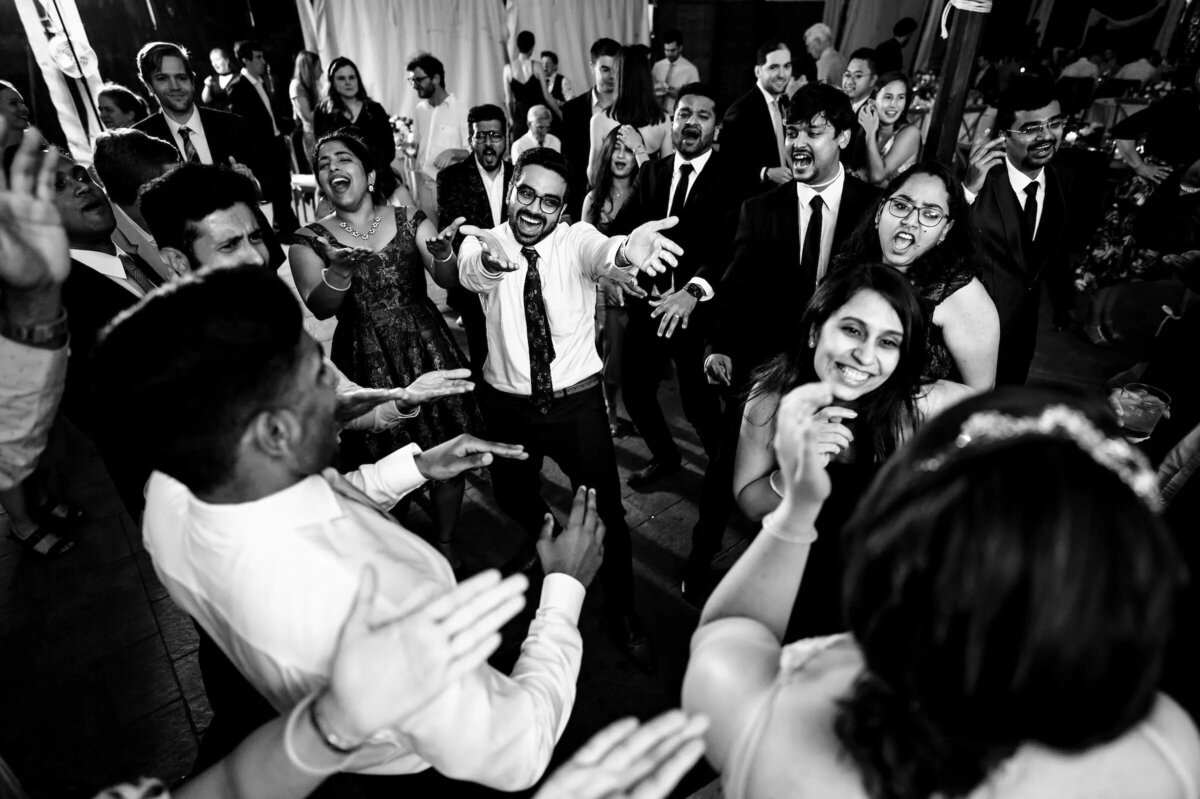 A lively wedding dance floor with guests clapping and reaching towards the bride and groom, capturing the excitement of the celebration.