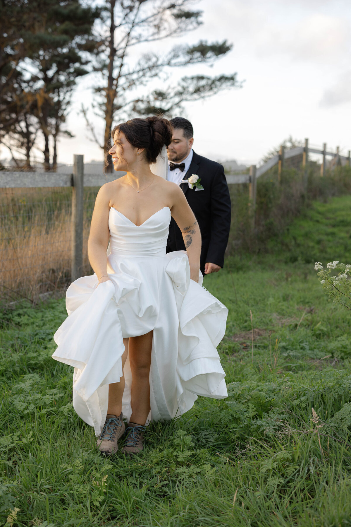 Bride and groom walking through tall grass during sunset hour