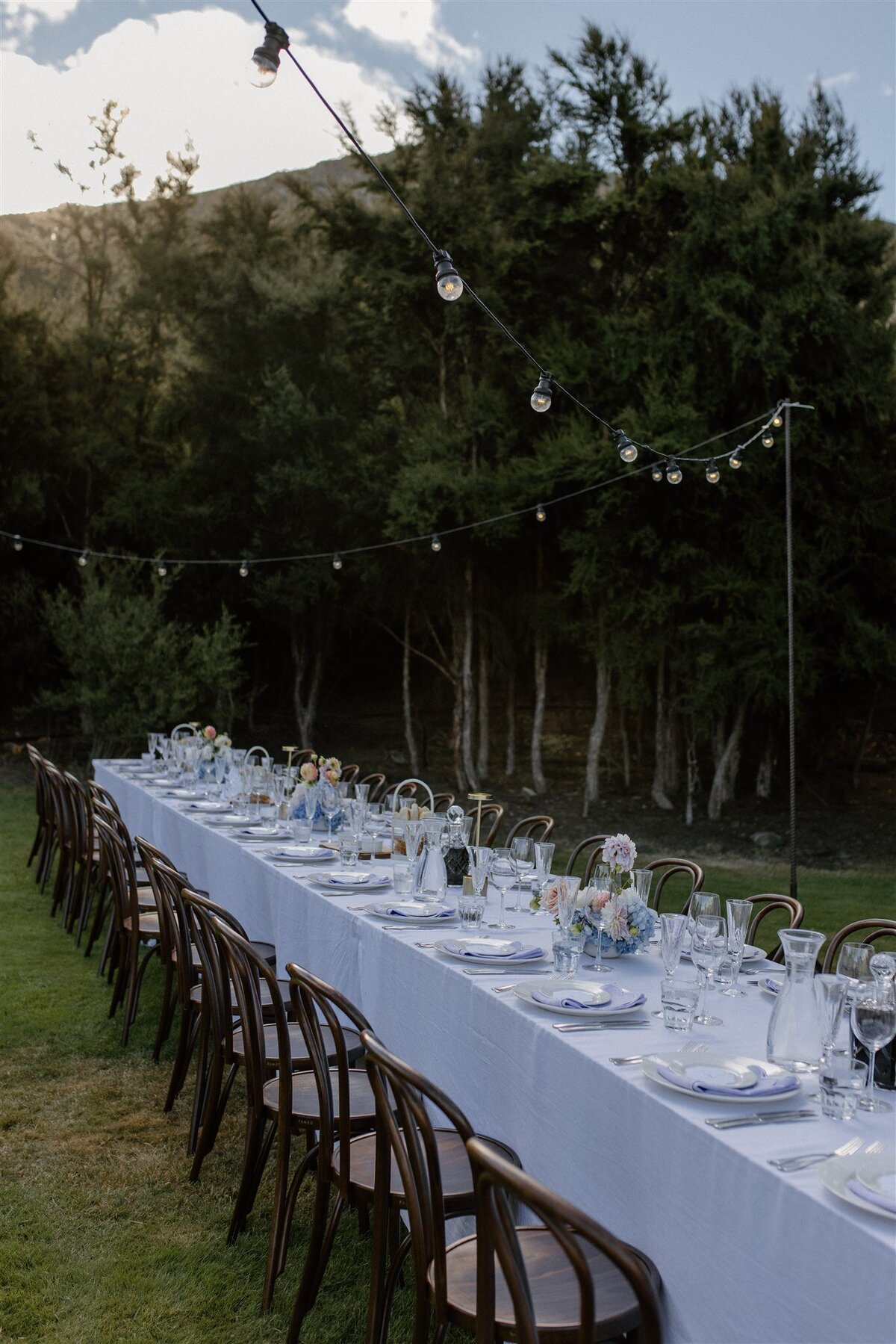 A matching wide-angle from the other side, showcasing long communal tables with elegant glassware, soft linen napkins, and dreamy pastel florals dotting the length of the tablescape.