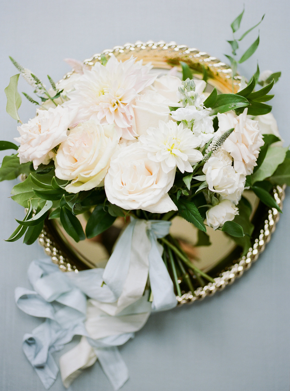 bridal bouquet with white roses and greenery on gold charger