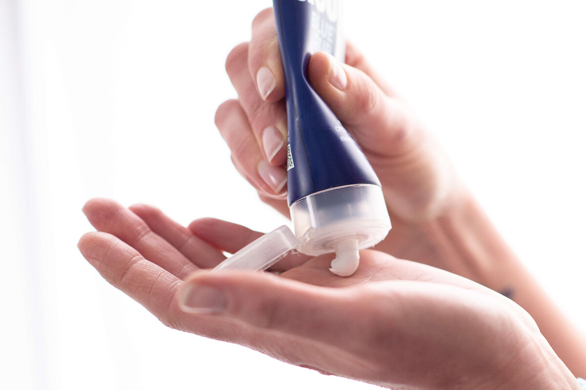 Ottawa branding photography showing a closeup of hands squeezing lotion out of a tube of DoTerra Deep Blue rub. Captured by JEMMAN Photography COMMERCIAL