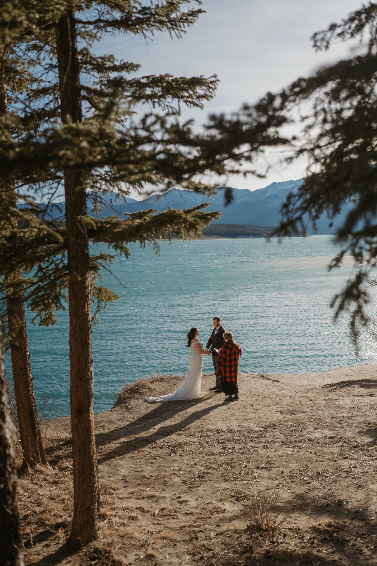 Private elopement wedding ceremony with bride, groom and officiant looking out over lake