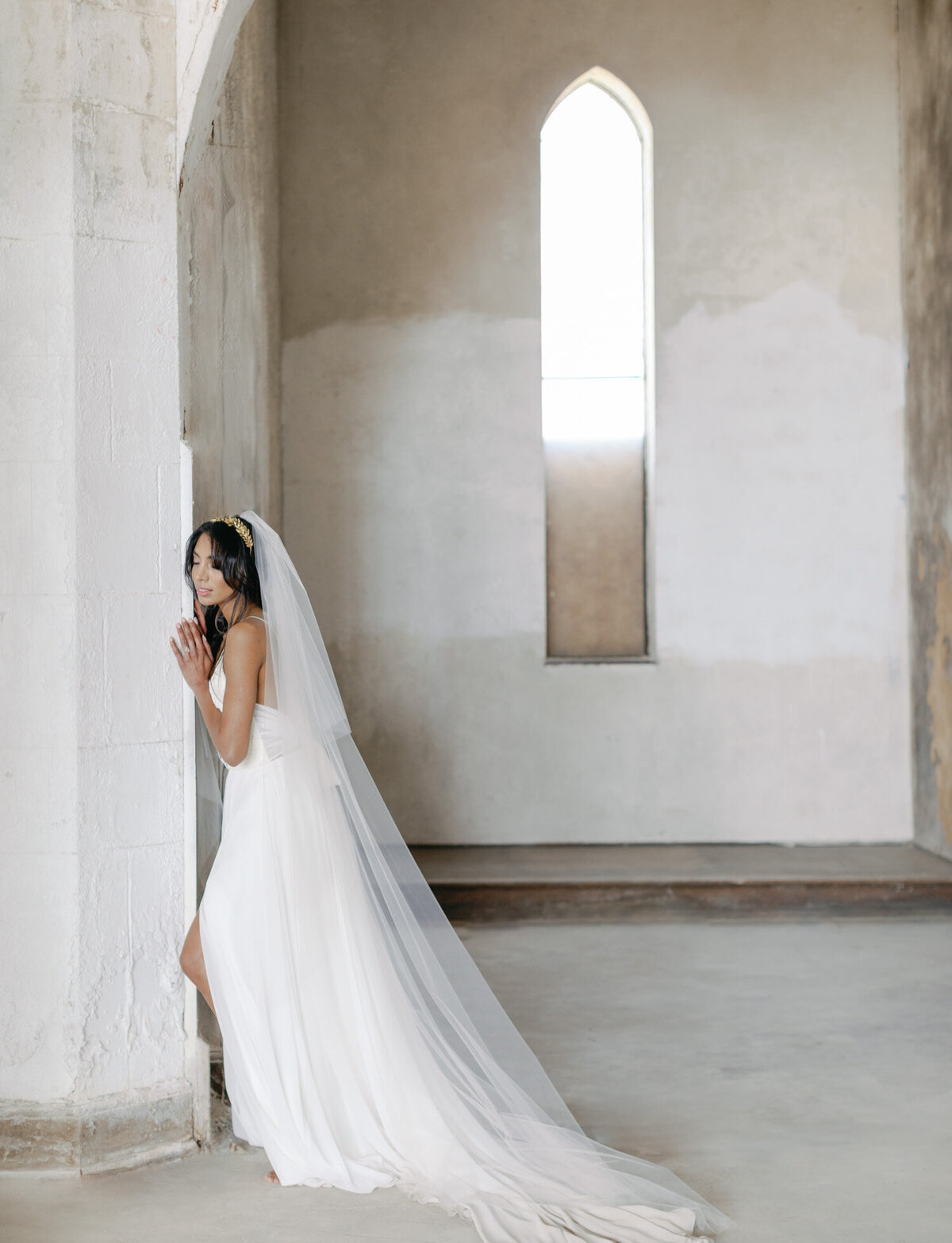 bride in long dress and veil leans on Mediterranean ruins, destination wedding in Italy, Croatia