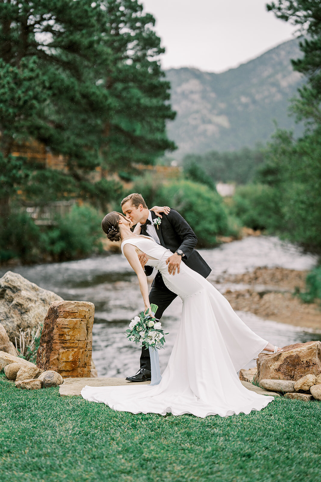 Bride and groom share a kiss flaunting her white and greenery floral bouquet after their ceremony at the Landing in Estes Park.