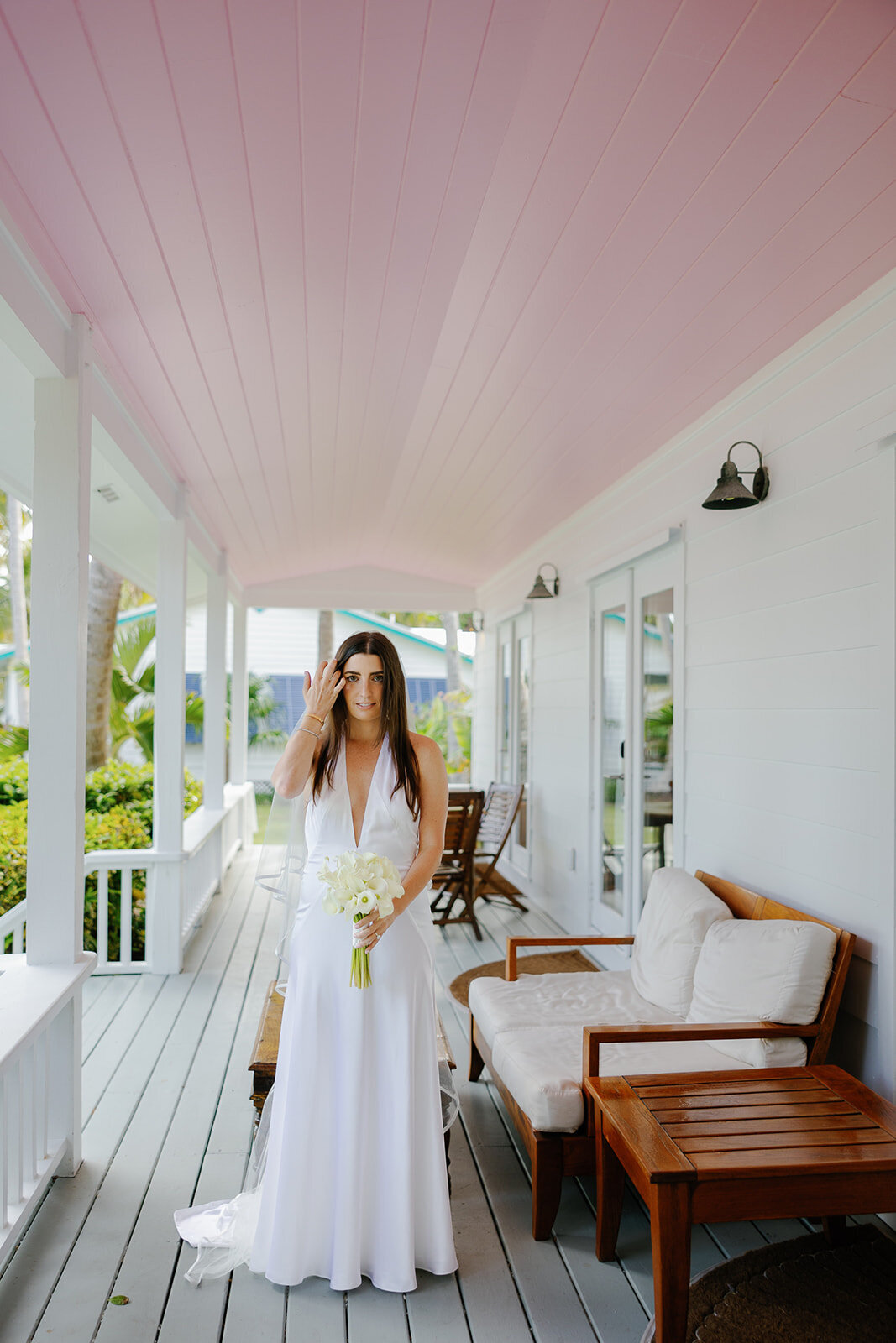 Minette looks stunning in her sleek wedding gown, holding a white bouquet on the porch of Casitas at Cheeca. Florida Keys micro wedding by Claudia Amalia Wedding Photography.