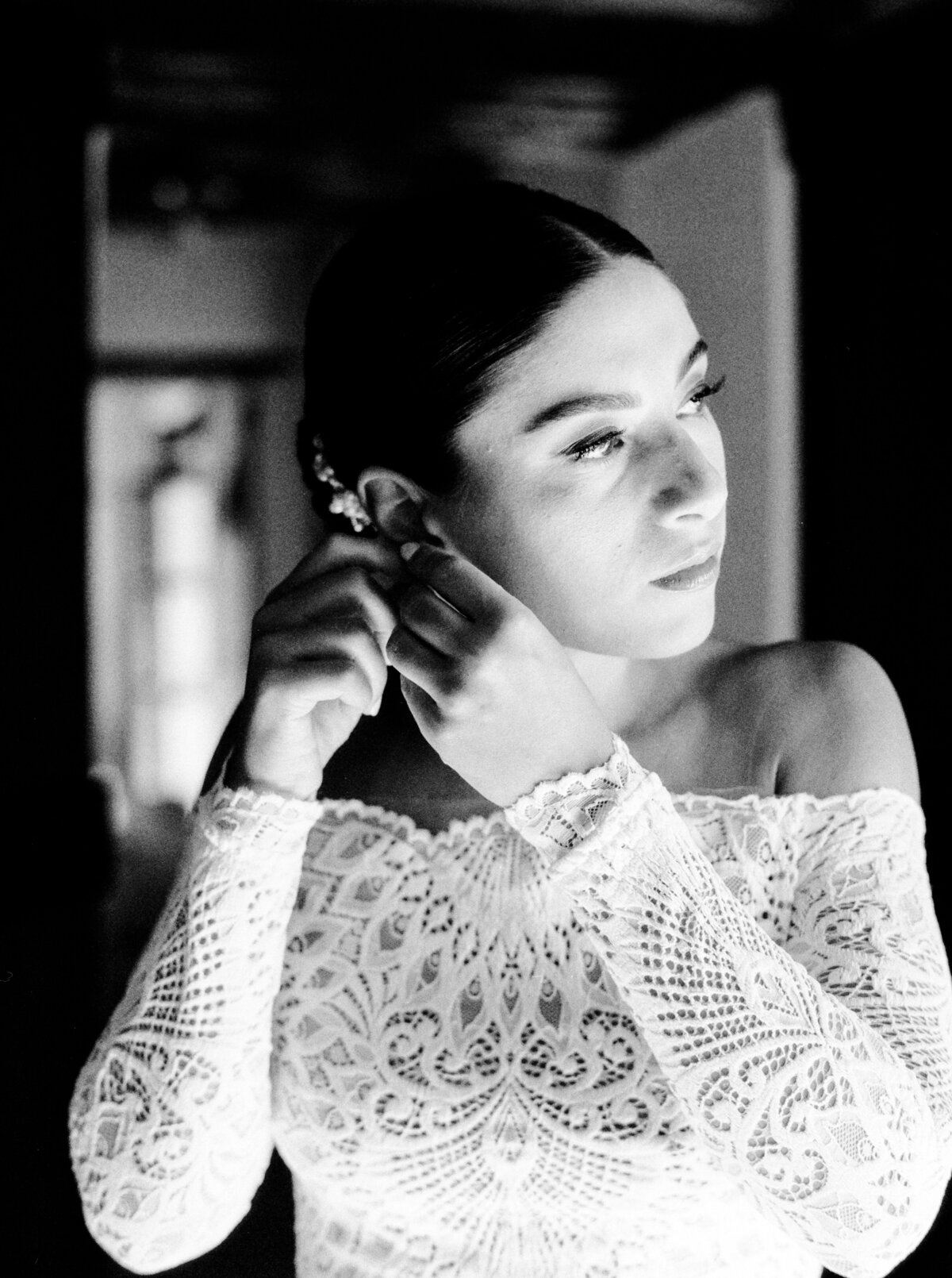 Black and white film photograph of bride in all lace wedding dress putting her pearl earring in photographed by Italy wedding photographer at Villa Montanare Tuscany wedding