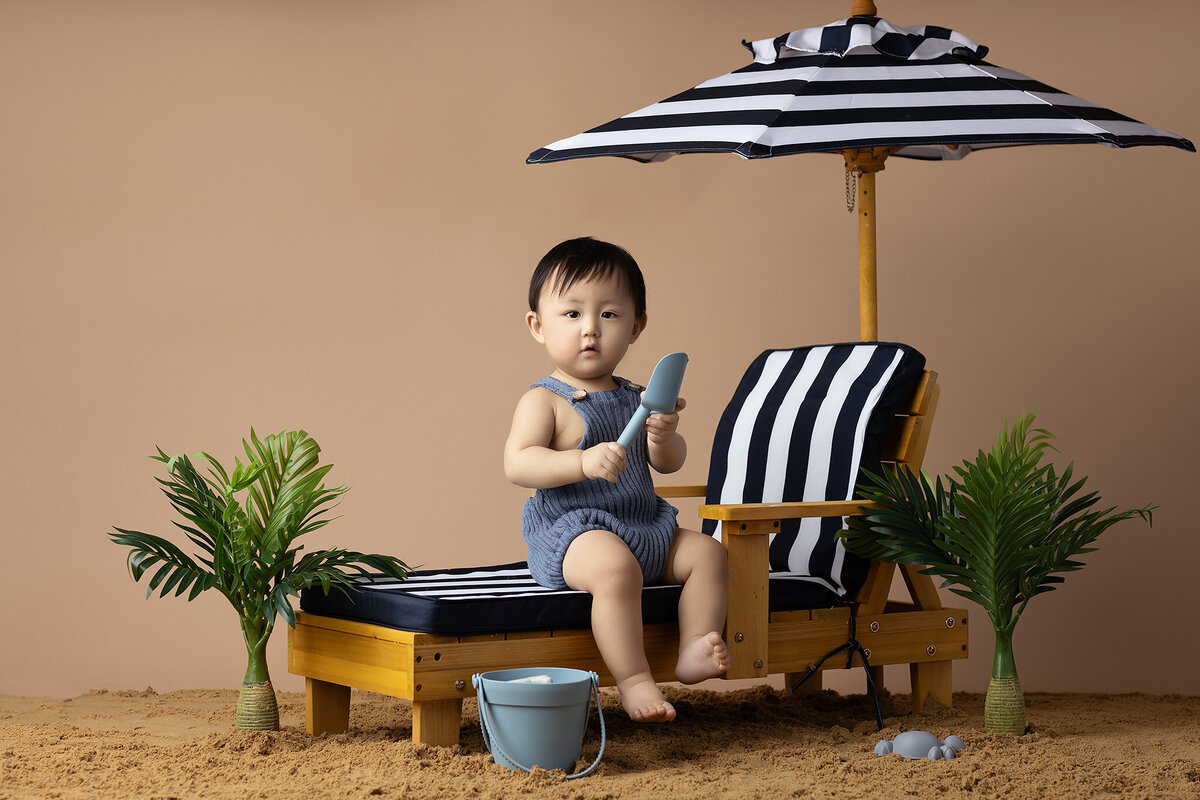 Dallas baby milestone photographer capturing a baby playing with a toy on a beach chair.