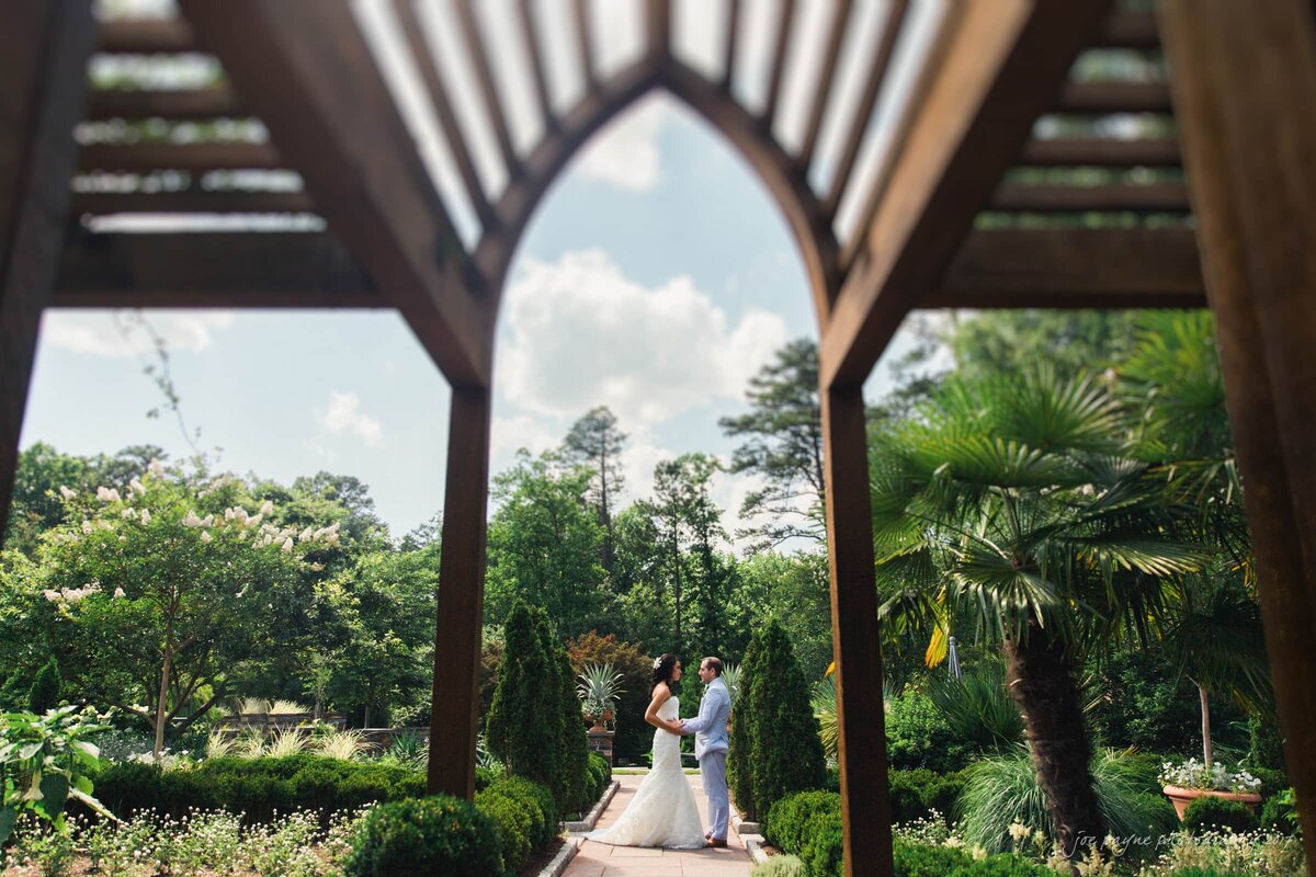 A wedding couple holding hands while standing in a garden area.