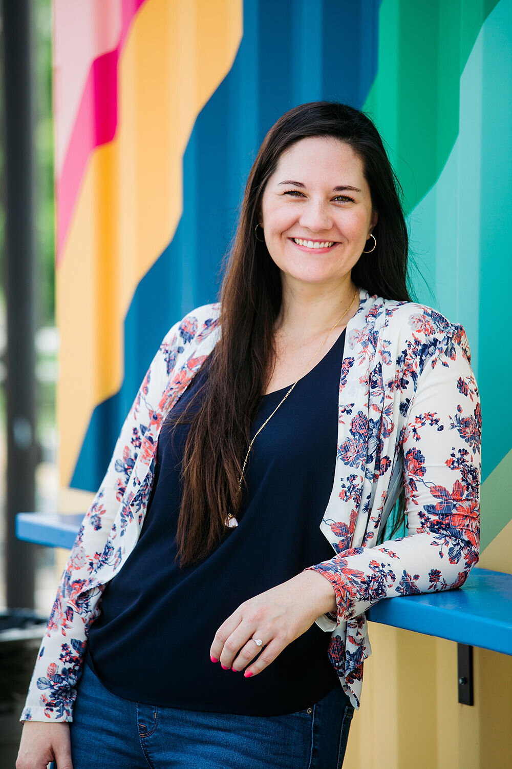 A woman leans on a blue table smiling.