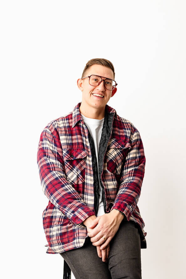 Man in red plaid coat folds hands and leans back in his chair during his photo session.