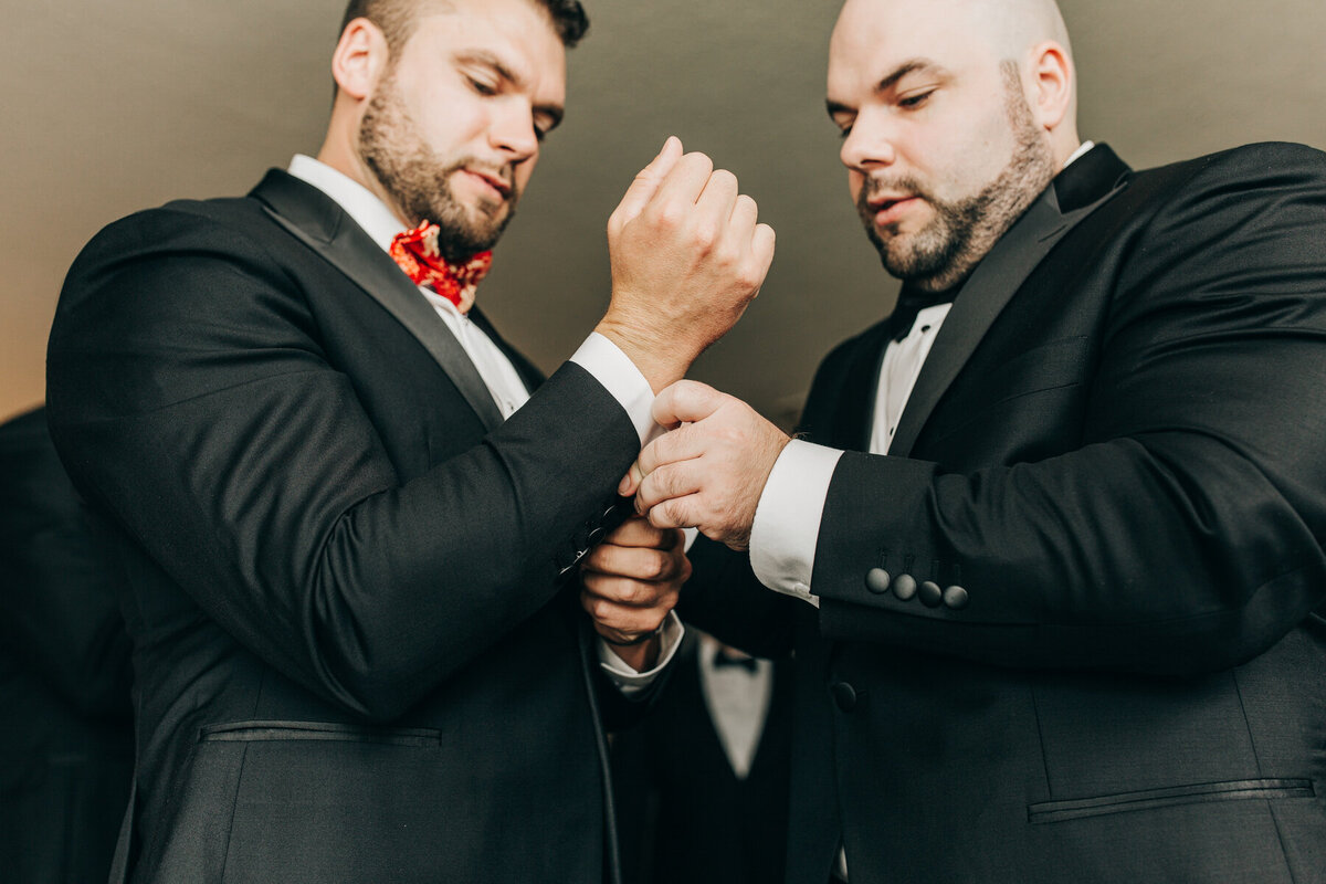 Groomsmen helping groom put on cuff links