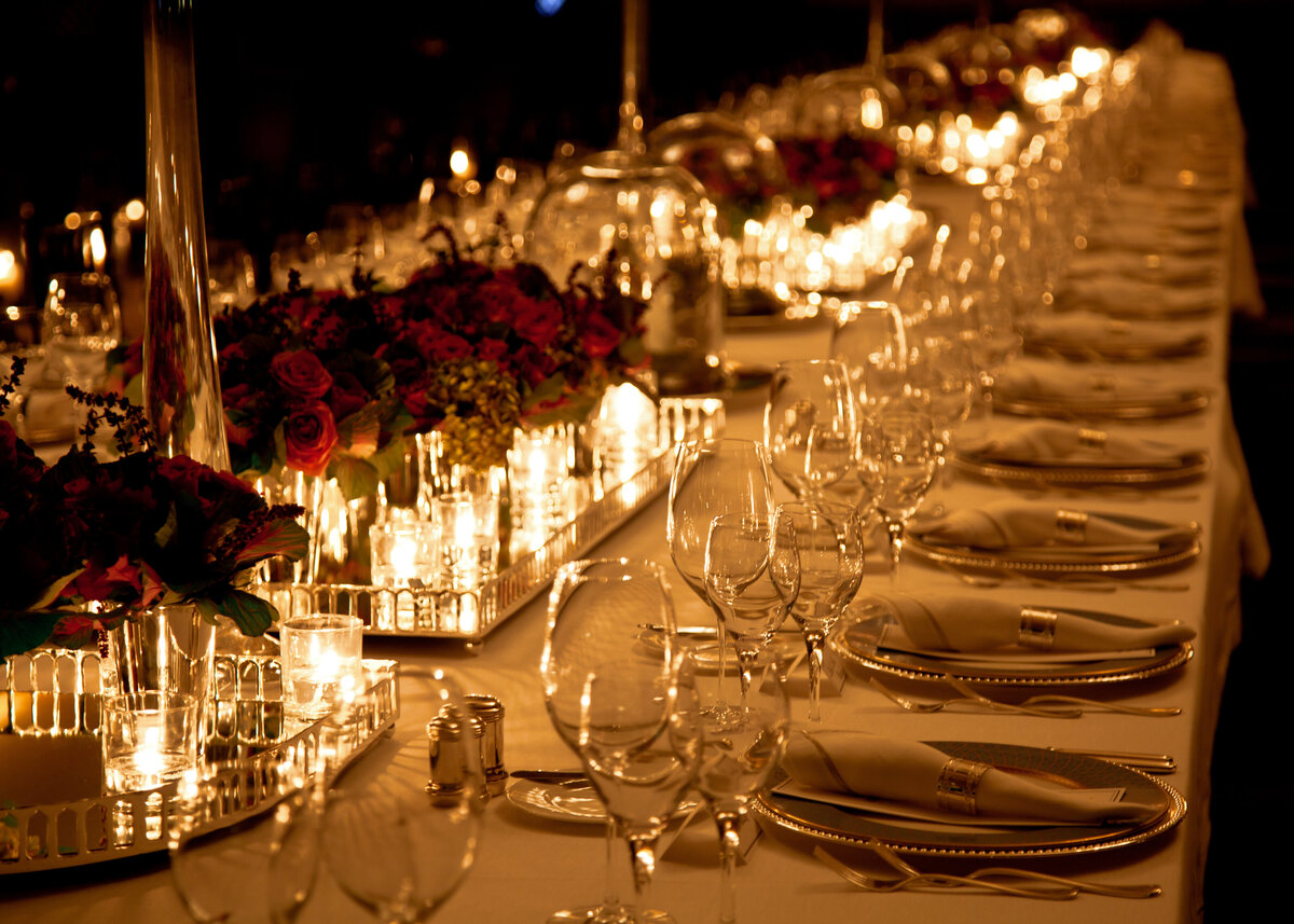 Elegant candlelight dinner table setting with red roses at a party.