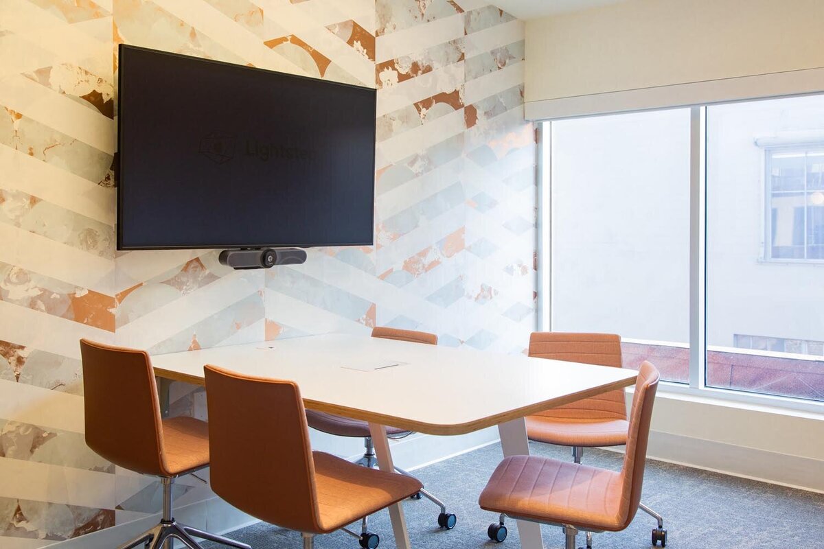 Small meeting room with patterned chevron wallpaper, a white table, and burnt-orange swivel chairs.