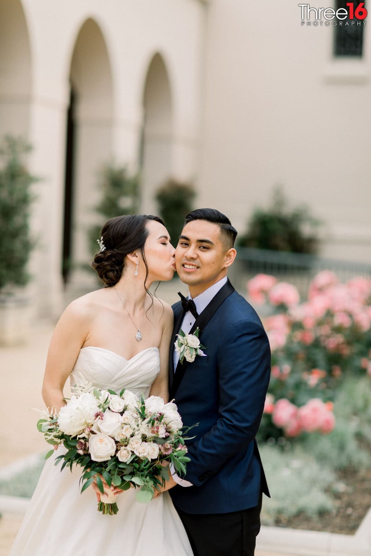 Bride kisses the Groom's cheek in the garden area of the NOOR