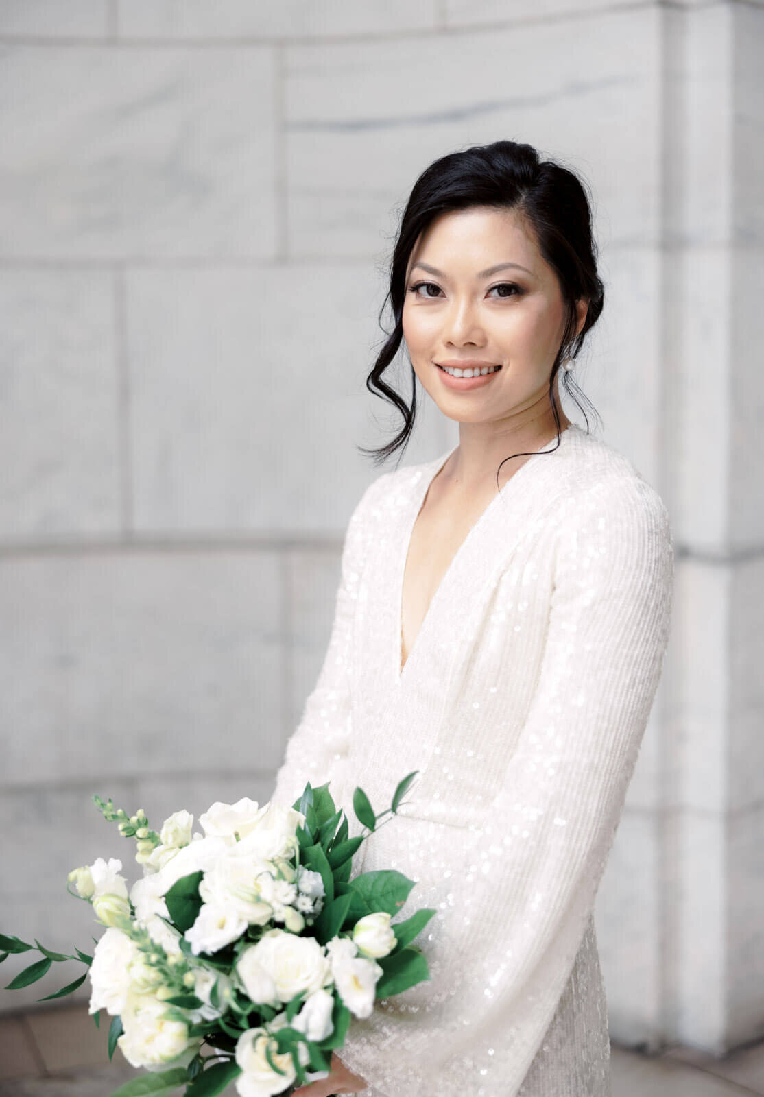 The pretty bride is holding her bouquet of white flowers inside the New York Public Library, NYC. Image by Jenny Fu Studio