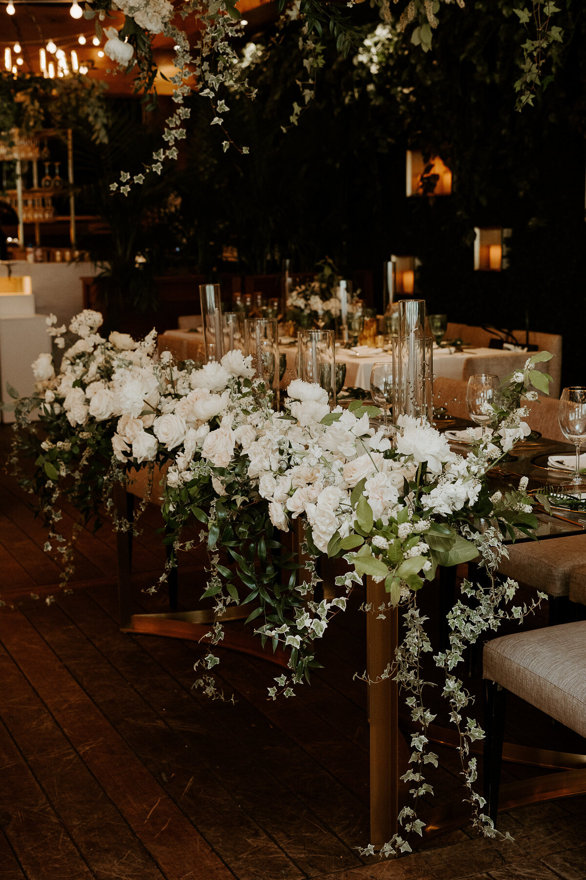 A sweetheart table at a Restaurant Beatrice wedding is lined with cascading greenery and flowers.